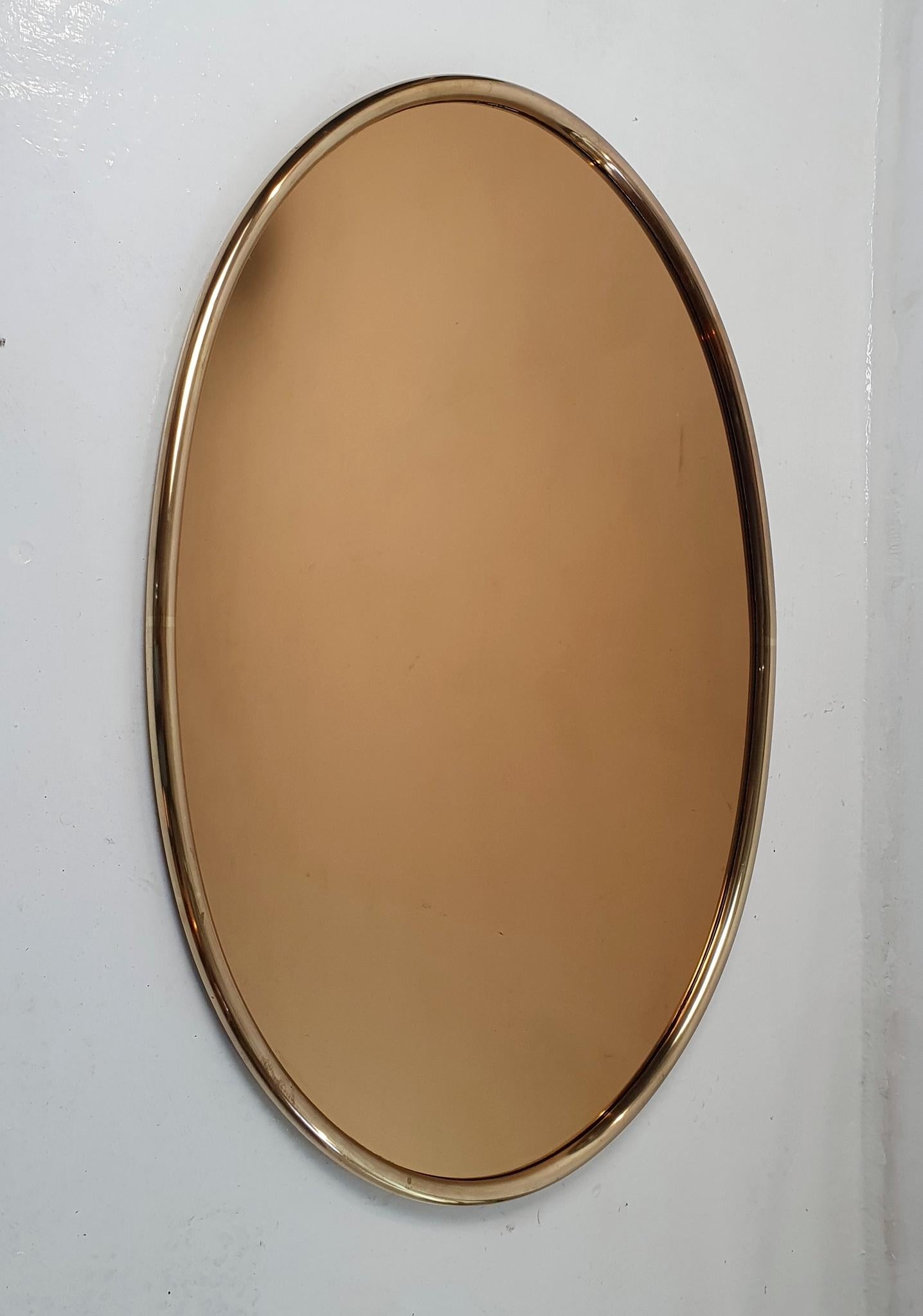 A gorgeous hand made Italian oval wall mirror designed from the 1960's in brass with a tinted original glass. The brass is solid and makes the mirror quite sturdy. The glass is in good condition.