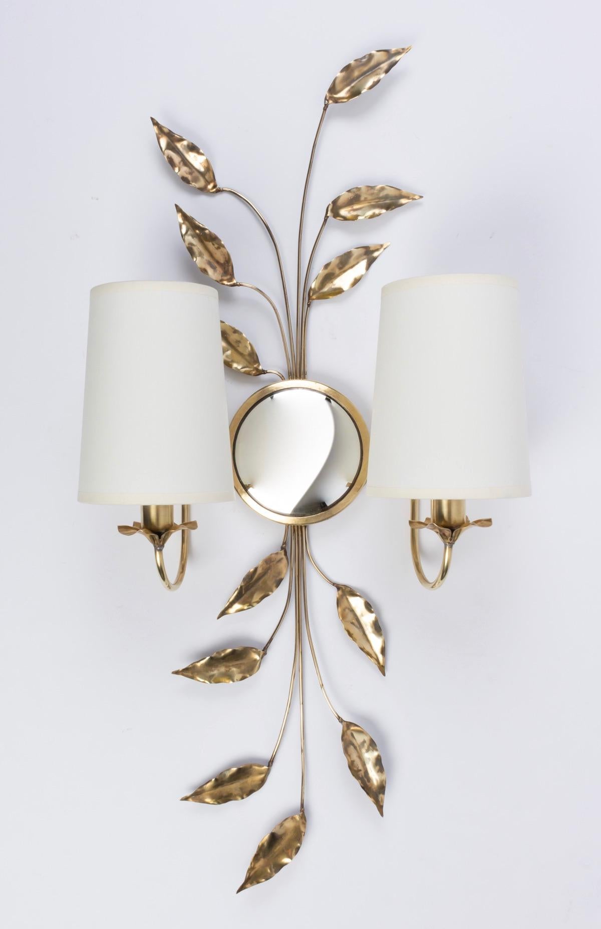 Charming creation from the 1970s by Maison Honoré. 
Each wall lamp is made up of two branches of rising and falling foliage attached together to a small round mirror surrounded by golden brass positioned in the center of the wall lamp.
On each side