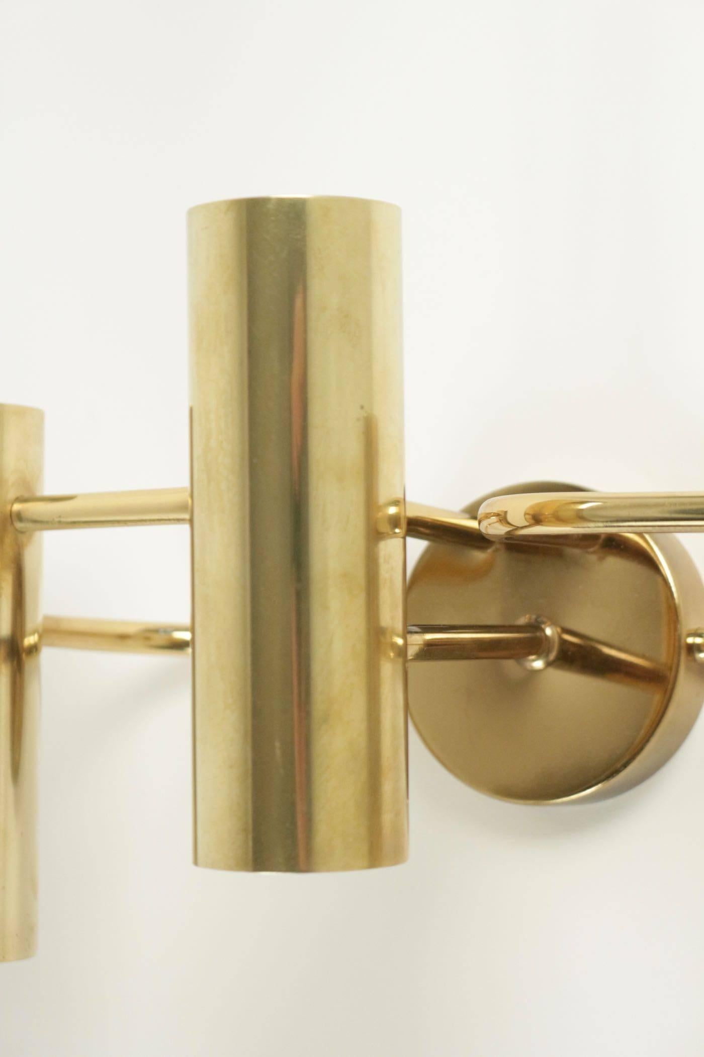 Pair of Gaetano Sciolari brass sconces from the 1960s.
The receptacles for three bulbs are made of three brass cylinders with brown patina effect mounted on curved brass arms.
Round wall plate.
Entirely in brass.

Three bulbs per sconce.