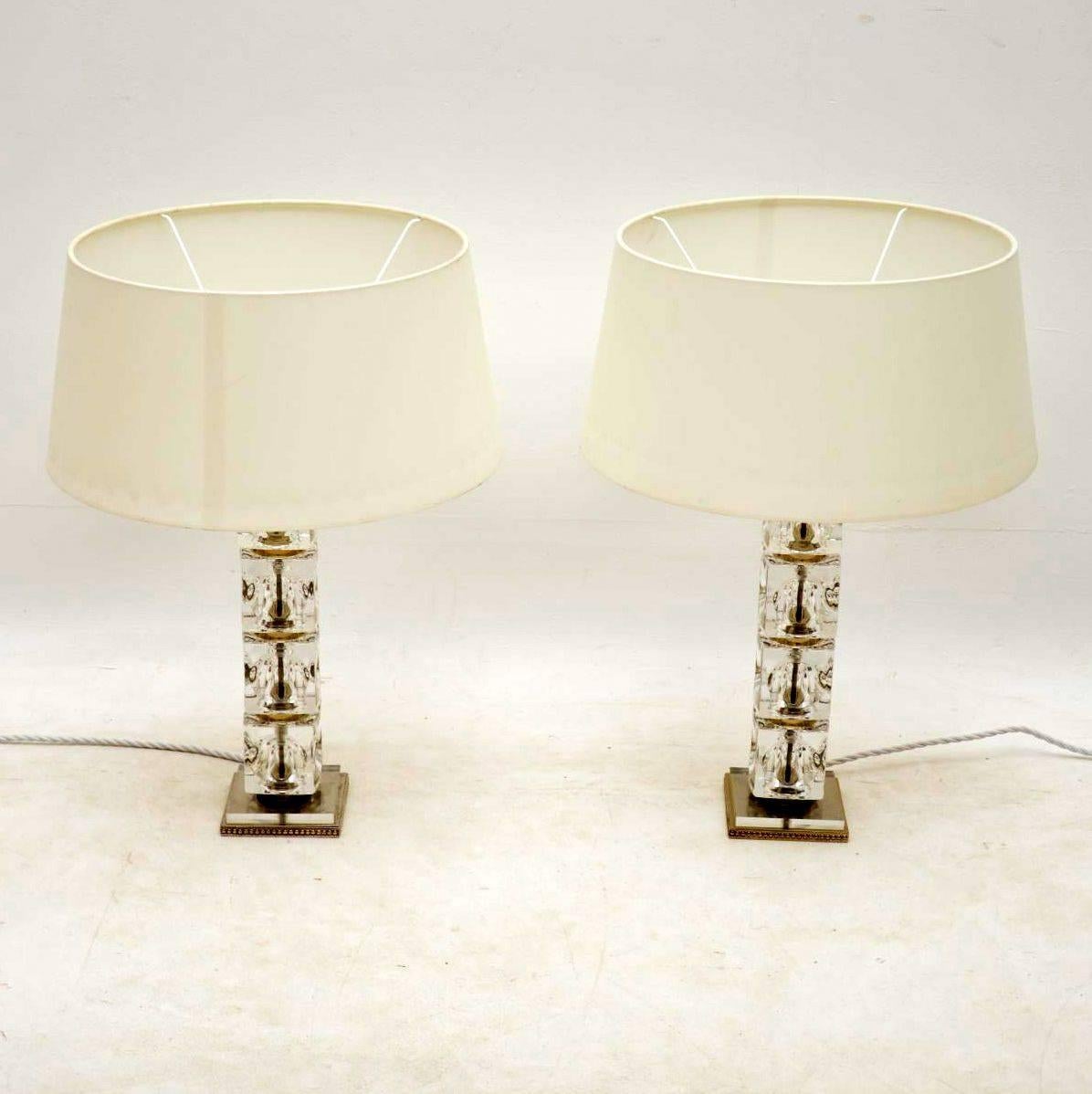 A stunning pair of vintage table lamps constructed from thick glass cubes with steel and brass trim. They are in superb condition for their age with only some extremely minor wear here and there. We have paired these with some lovely white shades