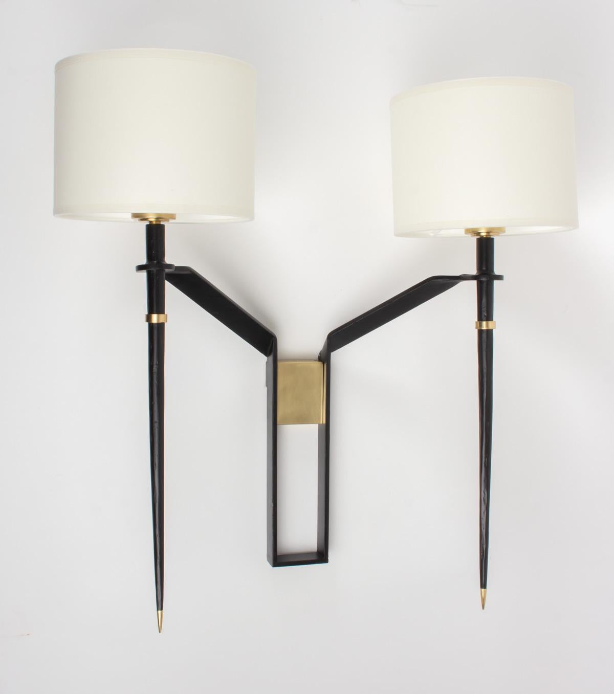 Elegant pair of Maison Honore sconces, French editions, 1960s.
Made of black lacquered wrought iron adorned with brass pieces.
Handmade off-white cylindrical cotton shades.
Two bulbs per sconce.
  