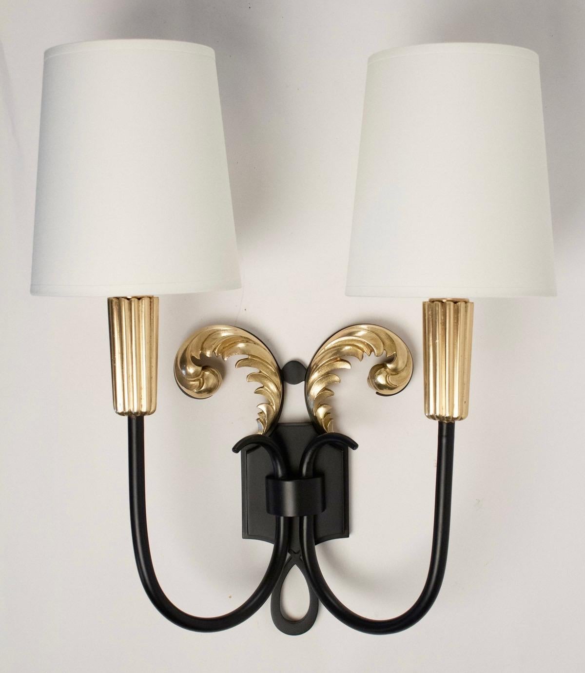 The back plate is adorned with two acanthe leaves made of gilded brass.
The two lighted arms are made of black lacquered iron and ended with brass fluted cups.
Handmade lamp shades of off-white cotton.