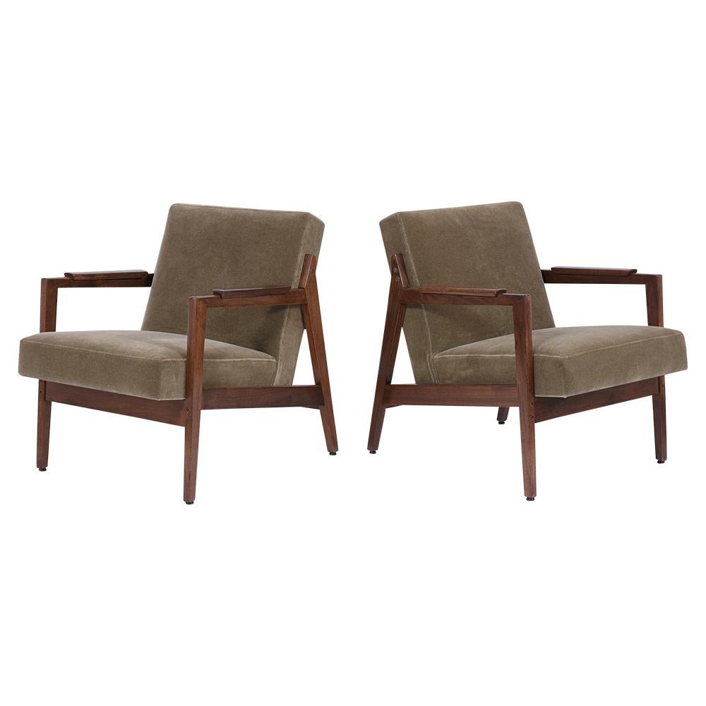 A pair of Mid Century Lounge Chairs handcrafted out of walnut wood and newly stained in mahogany color with a lacquered finish. The armchairs feature sleek carved frames, supportive slanted backrests, and have been professionally upholstered on a