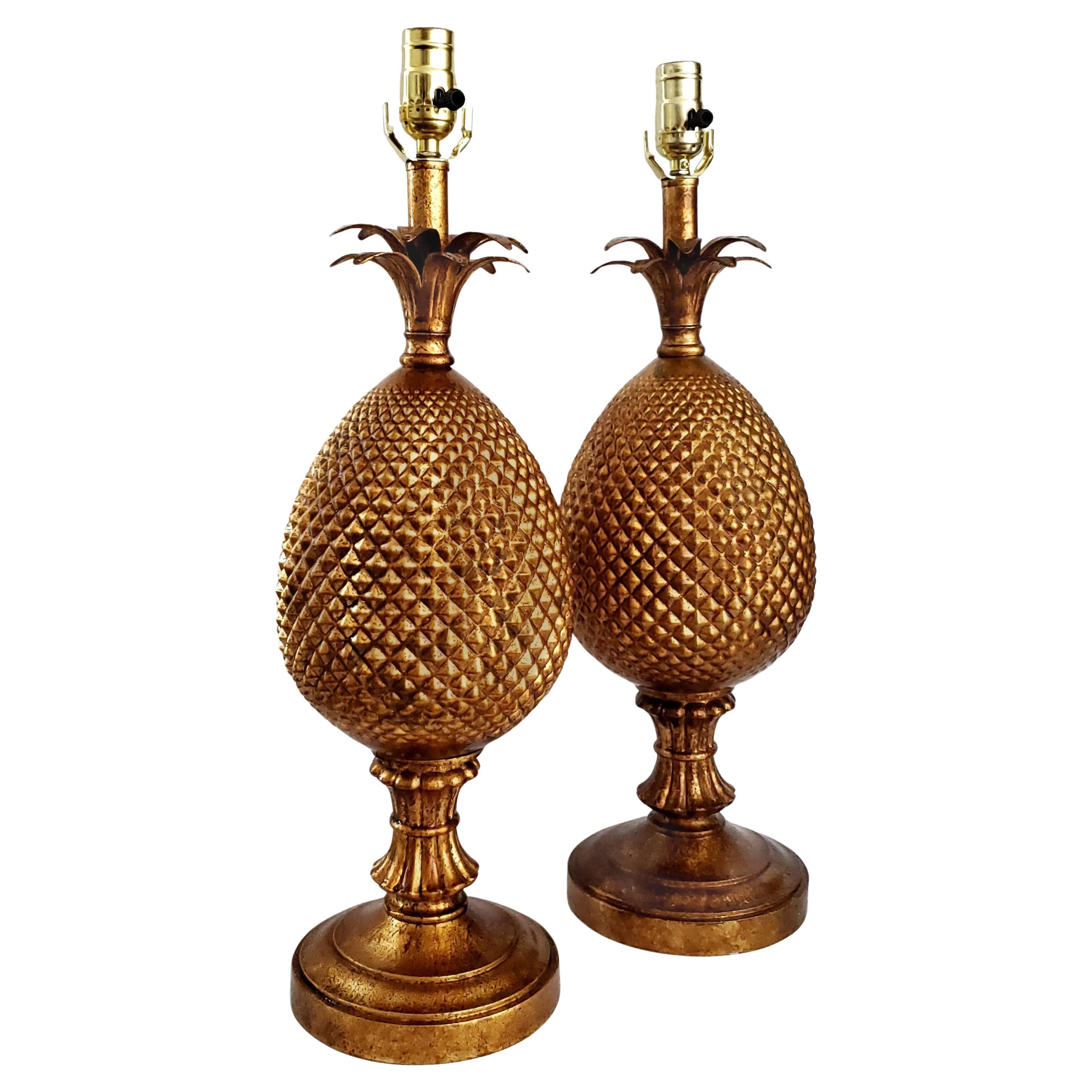 Pareja de lámparas de sobremesa vintage de metal en forma de piña con acabado de bronce antiguo, alrededor de los años 60. Estas lámparas monumentales representan una gran piña dorada posada sobre una base ornamentada y rematada con hojas de piña