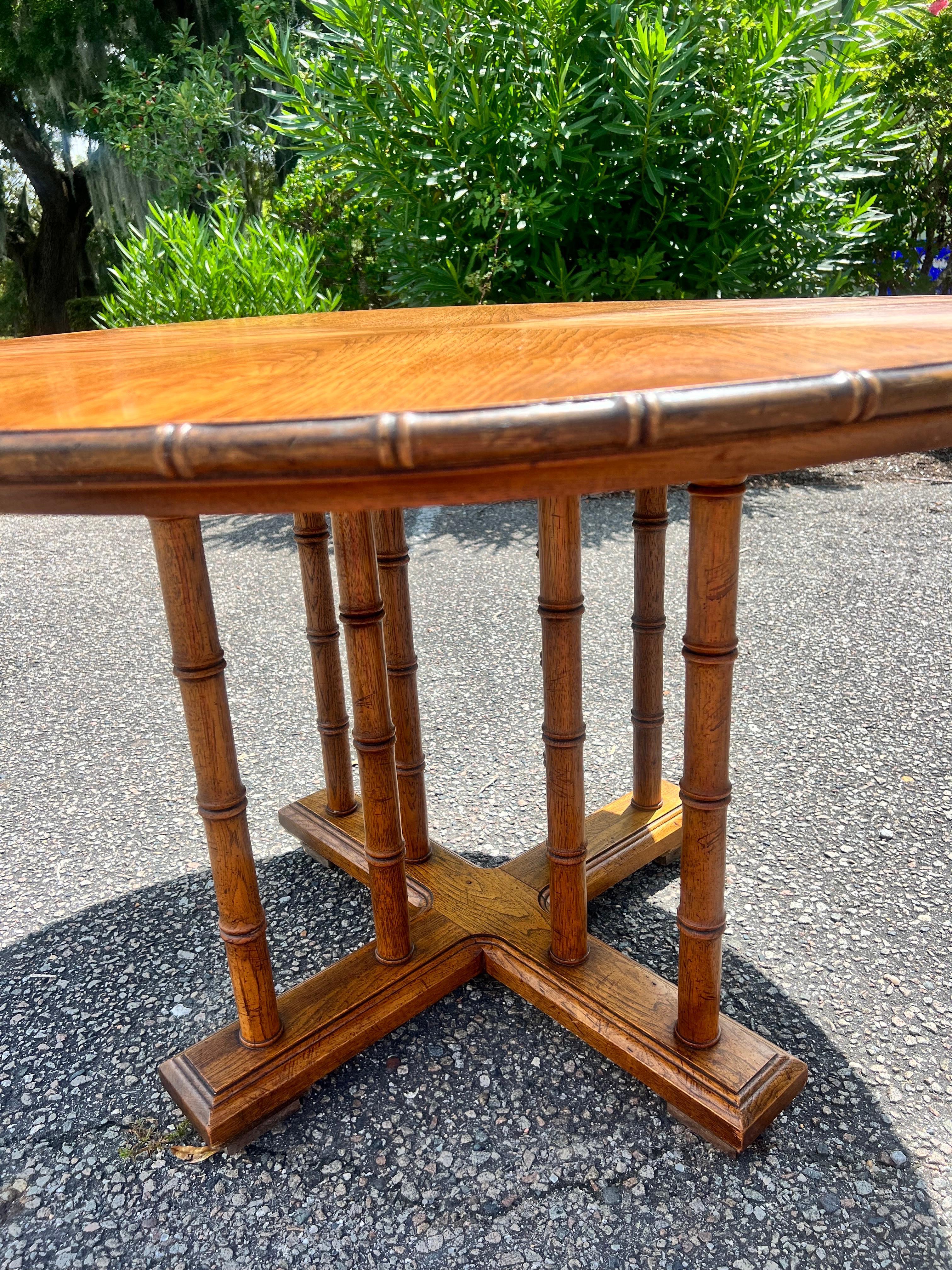 Vintage 1960’s pedestal base table with 2 faux bamboo spindles connecting the 4 feet to the table top totaling 8.    There is also a faux carved wood bamboo band around the table top.   The top has a very nice pie wood grain.