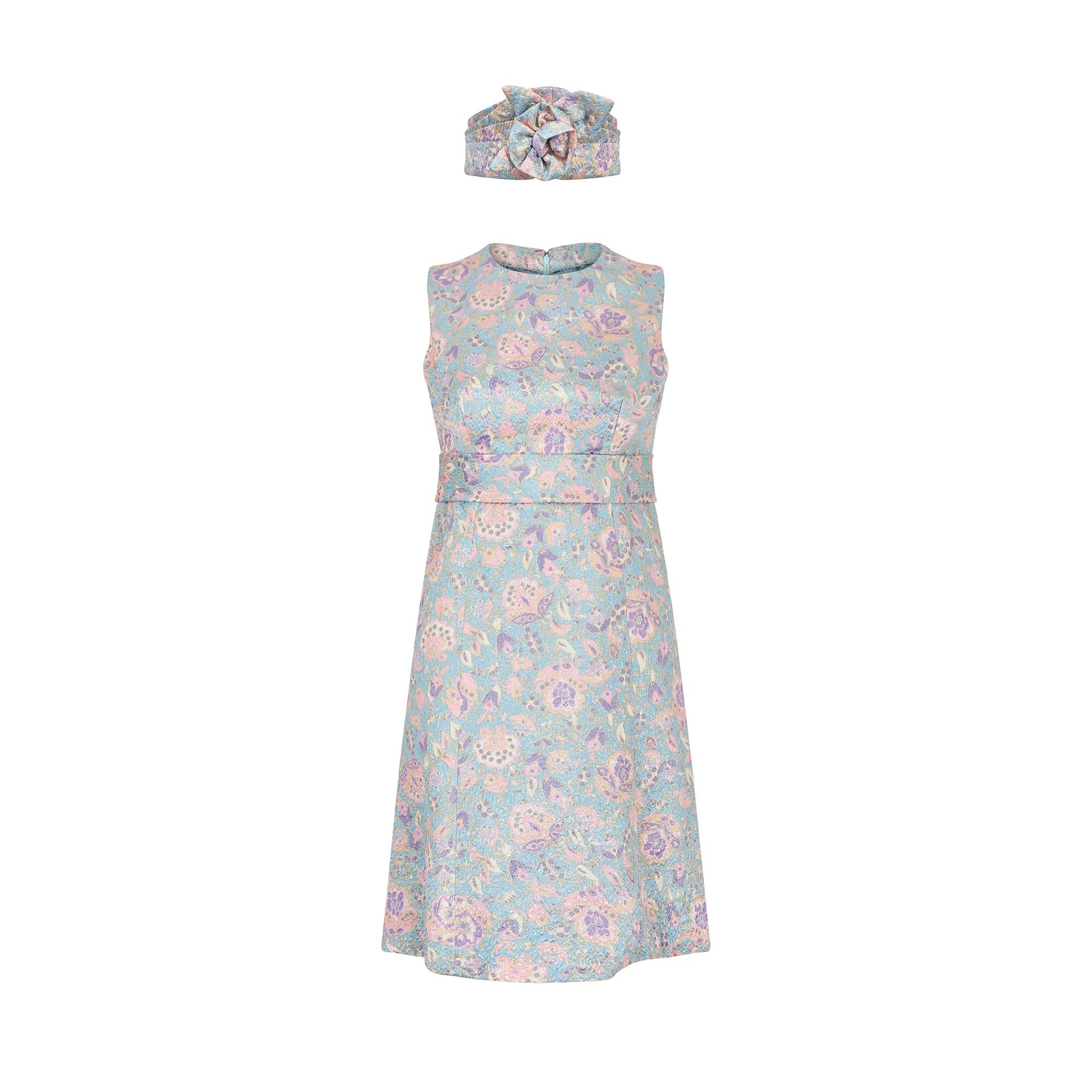 This French couture 1960s A-line mini dress has a wonderful luminosity to it thanks to its floral lame fabric. The neckline is high and softly rounded, and the interior is lined with a grey blue silky fabric. The exterior fabric is a silvery blue,