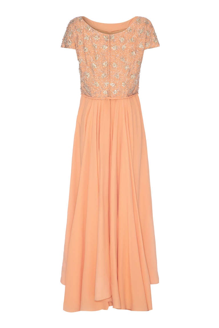 This enchanting 1960s peach silk crepe couture evening gown with beaded bodice is a beautifully elegant piece that we attribute to either Hardy Amies or Norman Hartnell. 
 I have handled dozens of couture pieces of both designers over the years and