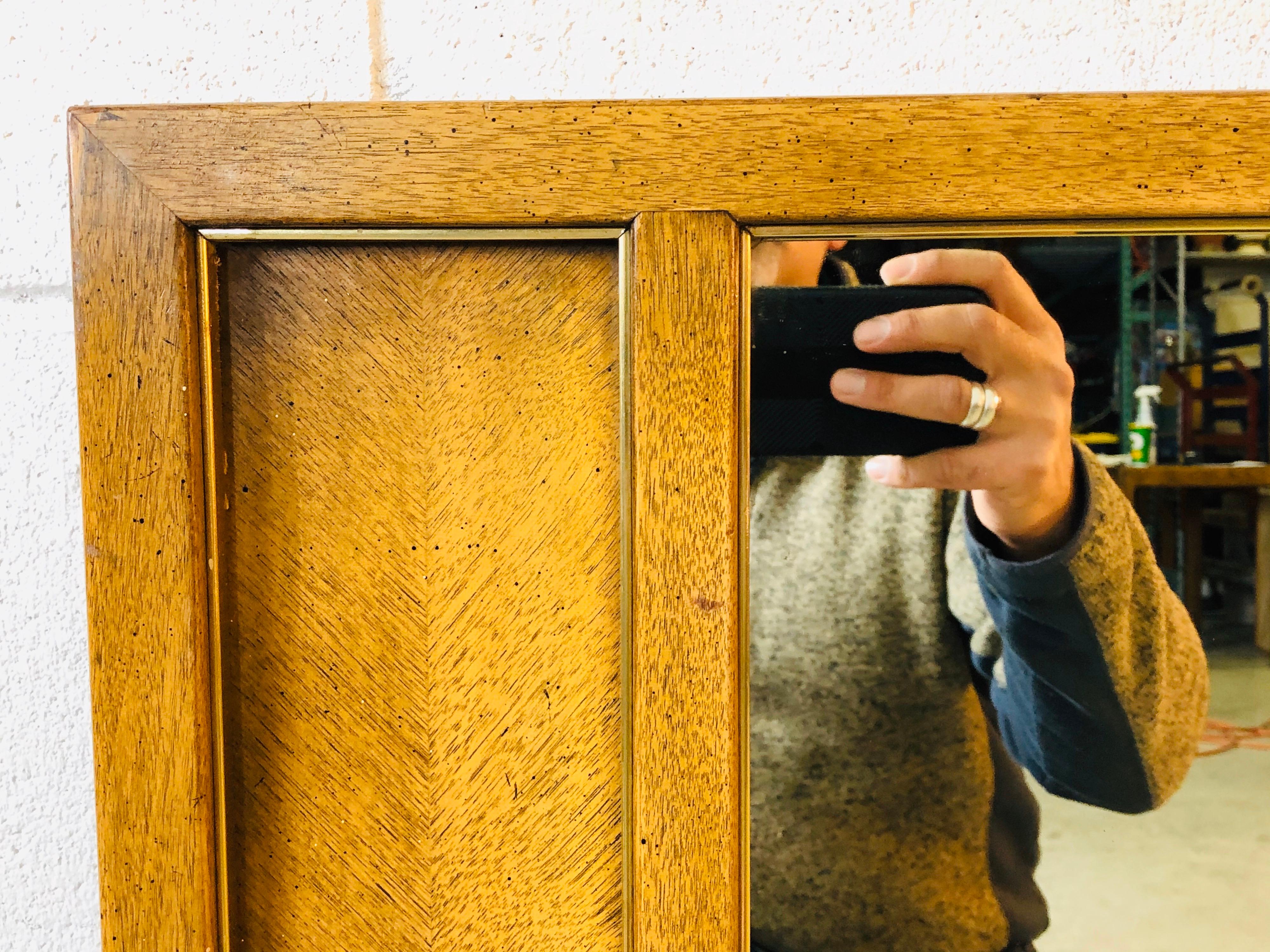 1960s rectangular wall-mounted mirror with a pecan wood frame and gold metal accents. Hook hardware provided. No marks.