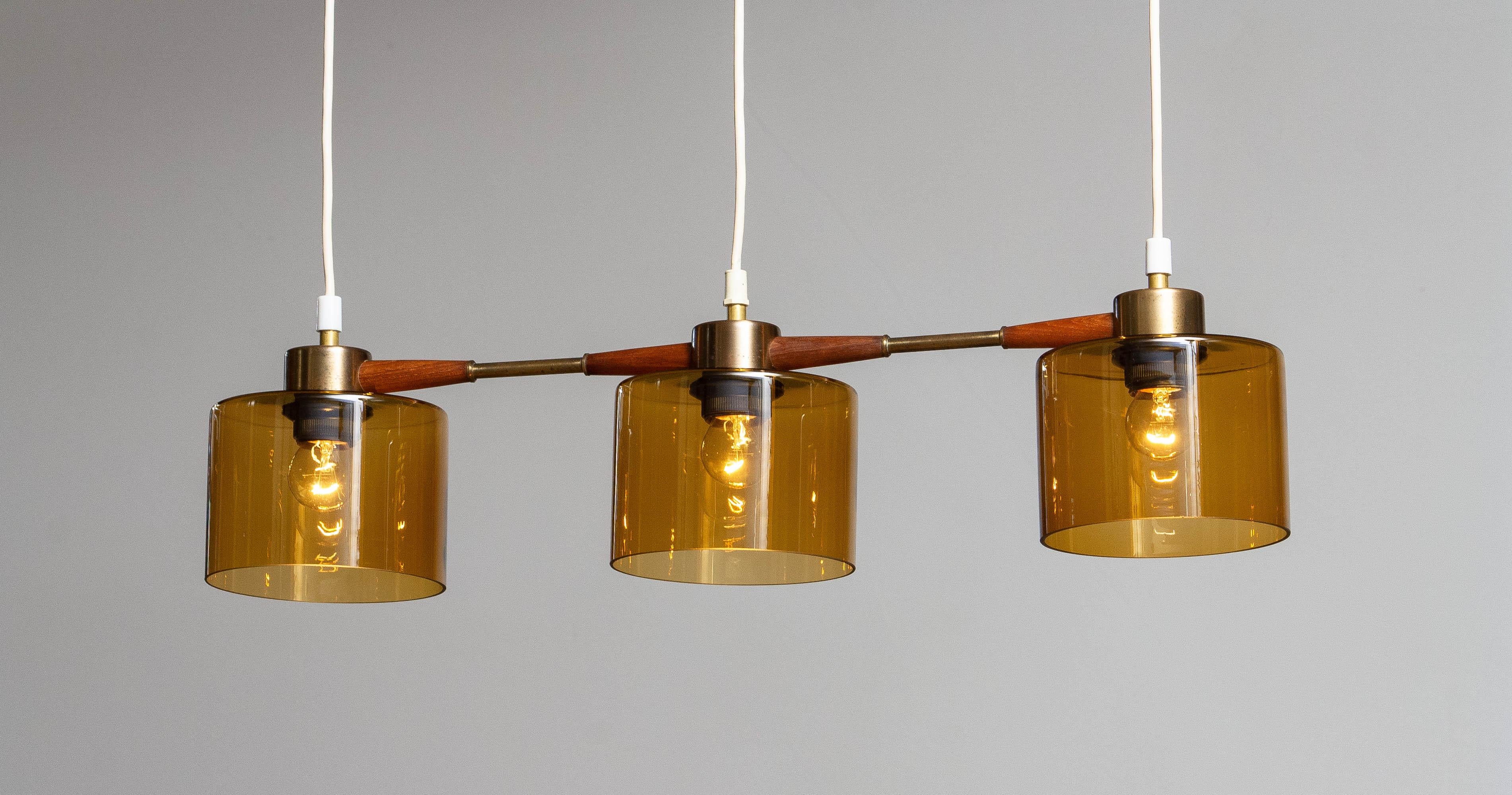 Beautiful three lights pendant with amber glas in combination with brass and teak designed by Carl Fagerlund for Orrefors Sweden.
In allover good condition.
Consists three screw fitting for E26 / 27 screw bulb.