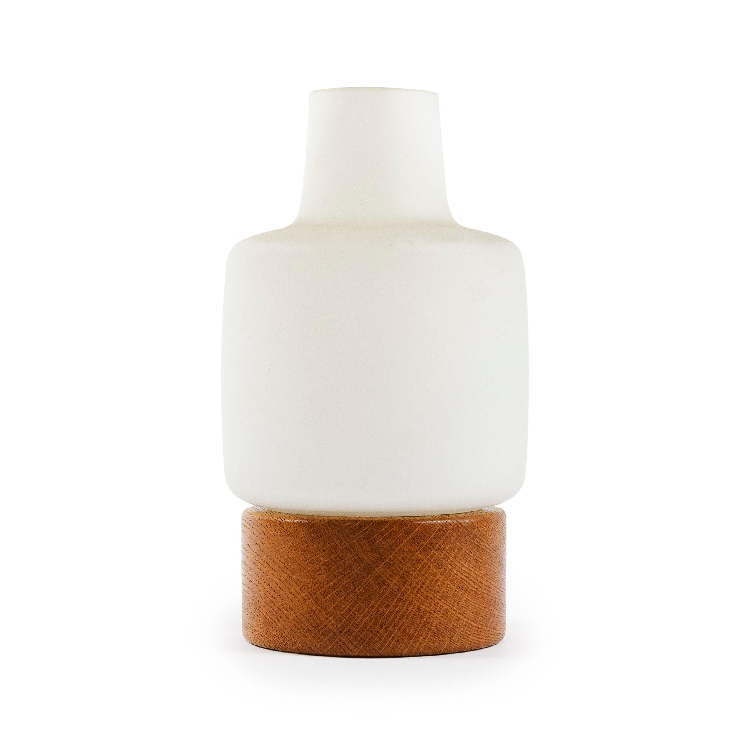 A petite table lamp with a white matte translucent glass shade resting on a rounded oak base.