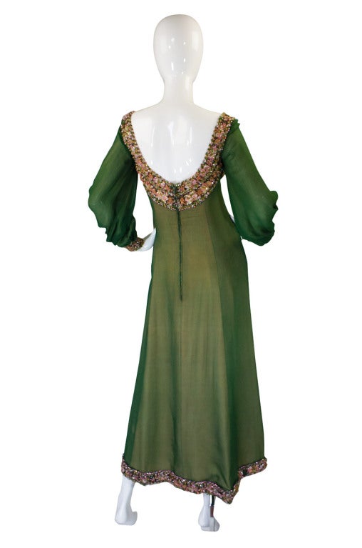 This stunning dress is a numbered haute couture gown by Balmain. It is a fantastic blend of green silk chiffon that is layered over a pale pink base. The effect of the two colors together is quite beautiful. The bodice, cuffs and hem are all heavily