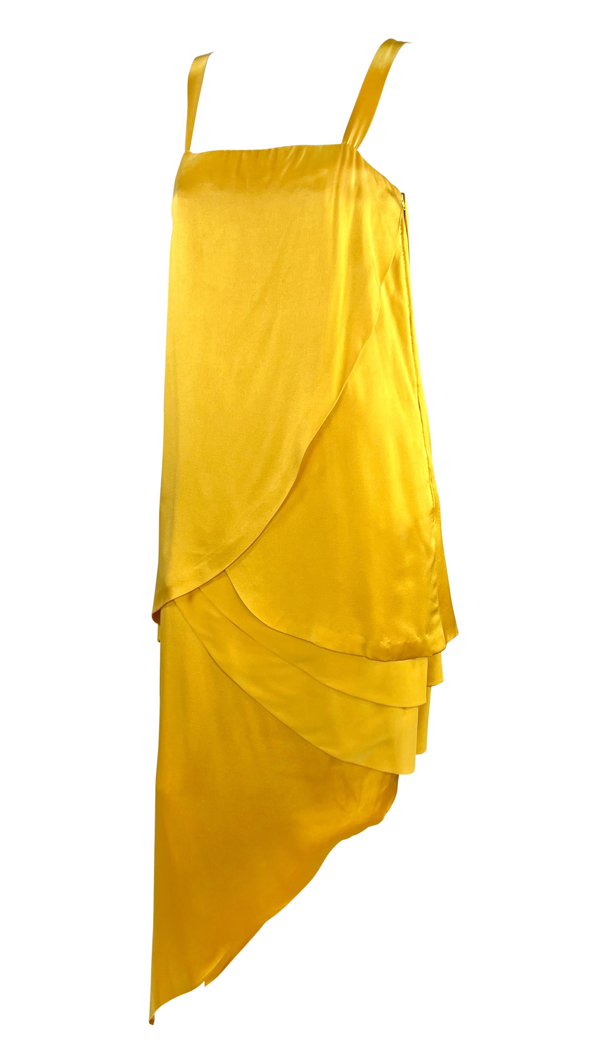From the 1960s, this tiered Balmain Haute Couture asymmetrical gown is constructed entirely of luxurious marigold yellow silk satin. This classic dress, entirely handmade by world-class artisans, features a sweeping tiered design that leads to an