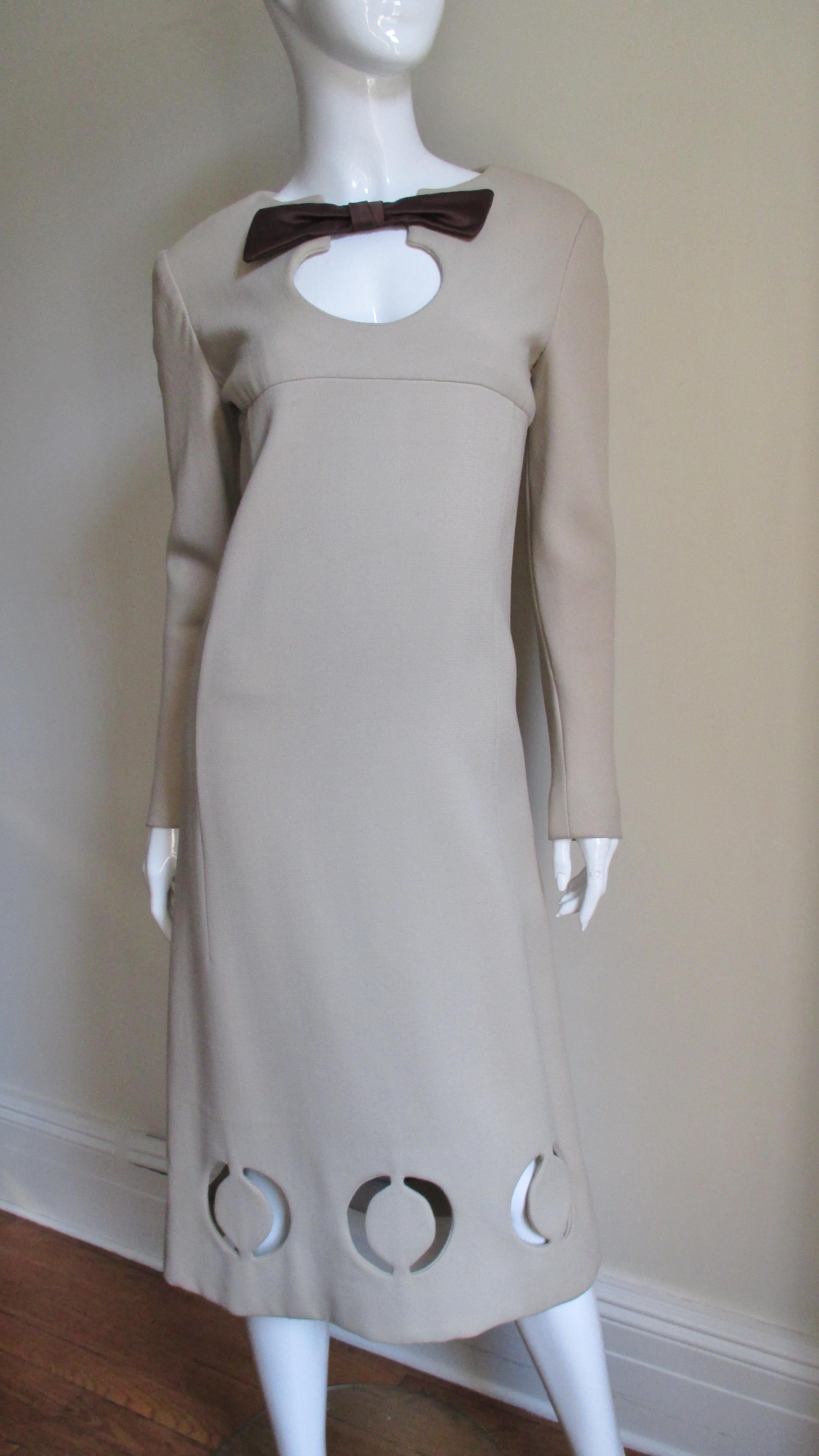 A fabulous dress from Pierre Cardin in light taupe wool.  It has front and back yokes, long sleeves, and a crew neckline with a silk bow at the top of a circular cut out.  The dress slightly widens towards the hem where there are detailed circular