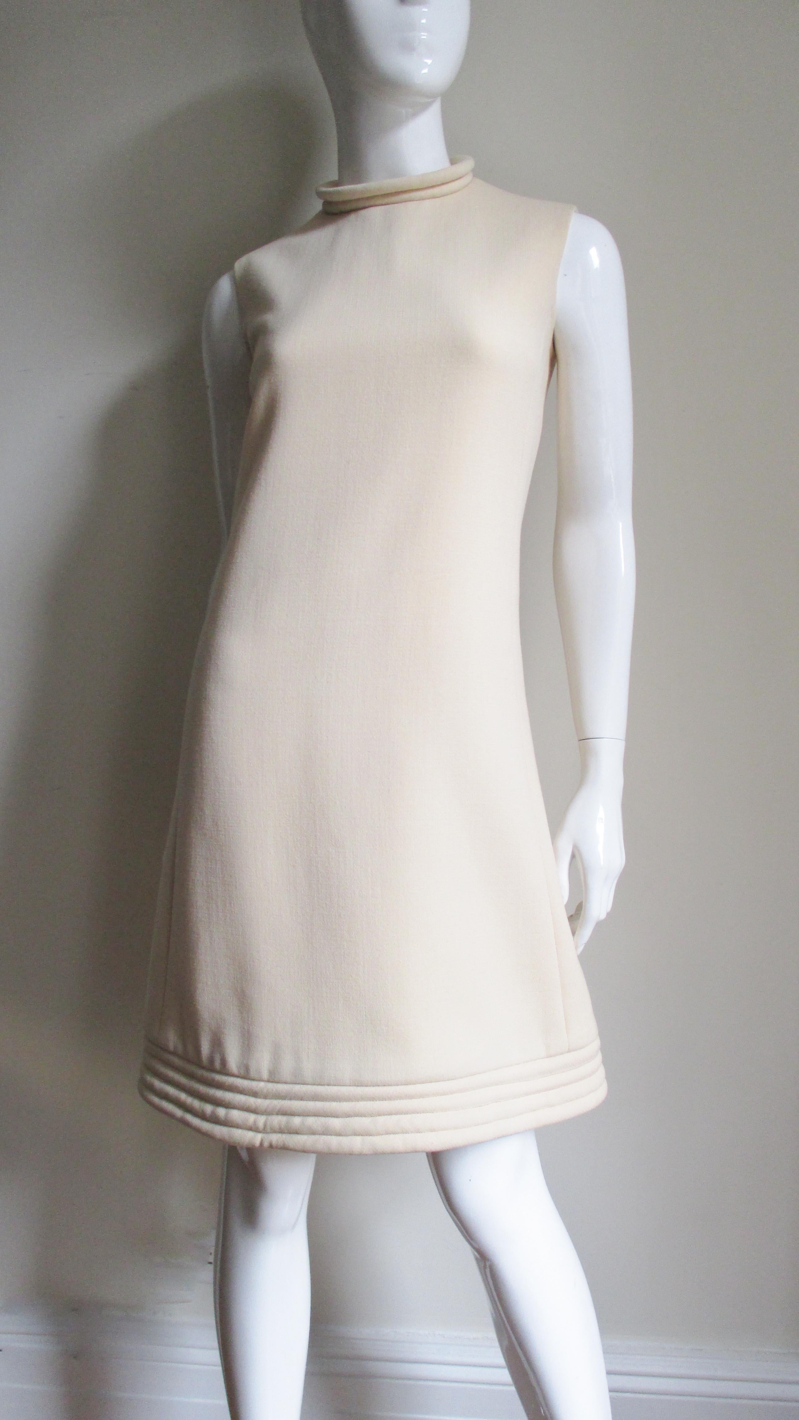 A fabulous off white wool dress by Pierre Cardin. It is an A line sleeveless dress with a stand up collar and hem highlighted with rows of top stitching around their circumferences.  It is lined in off white and has a center back hand sewn metal