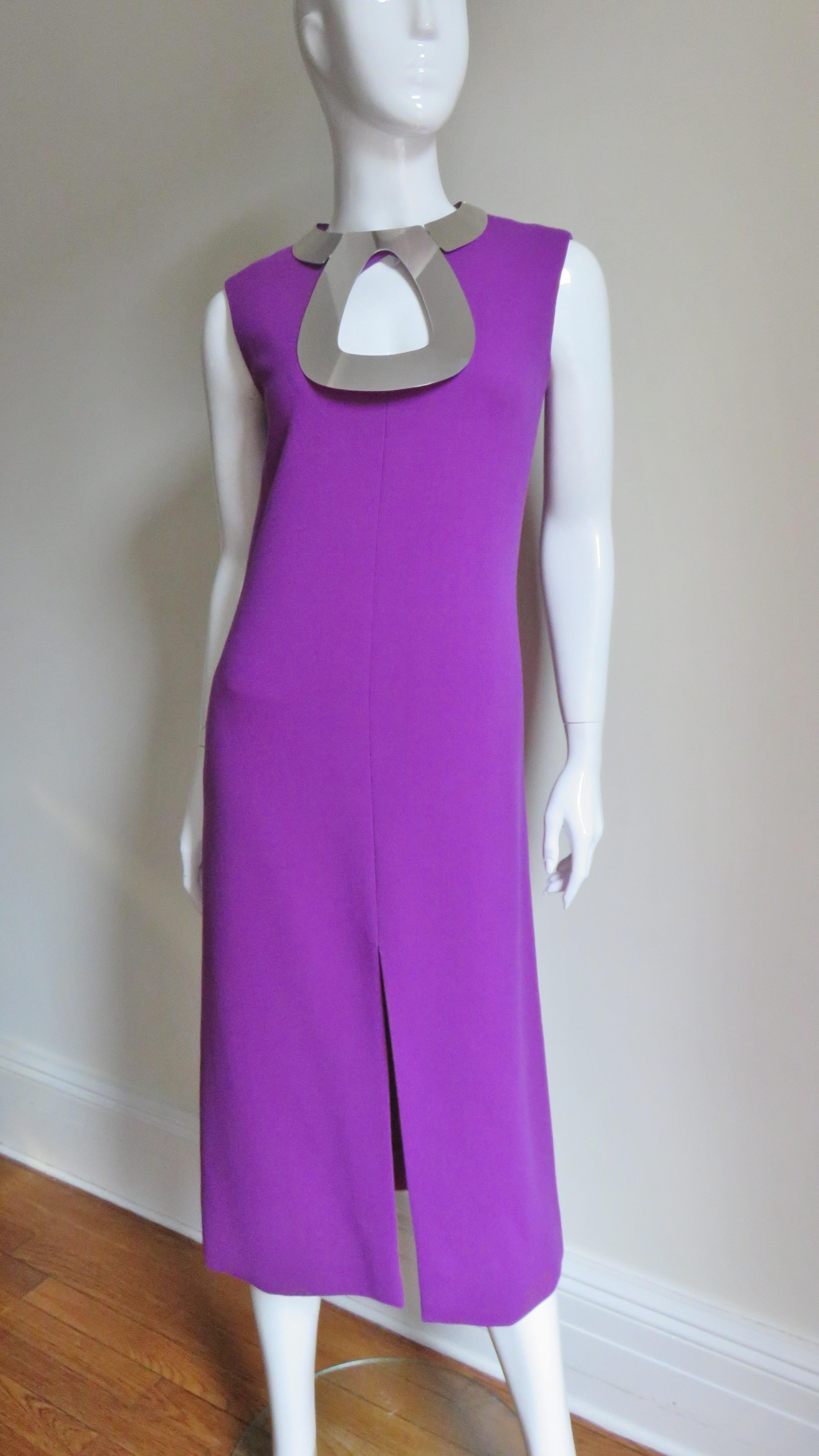 An amazing purple wool dress from Pierre Cardin.  It is sleeveless, skims the body then flares subtly to midi length with a center front slit.  Around the neckline is a stunning silver metal hardware articulated collar framing the neck and a large