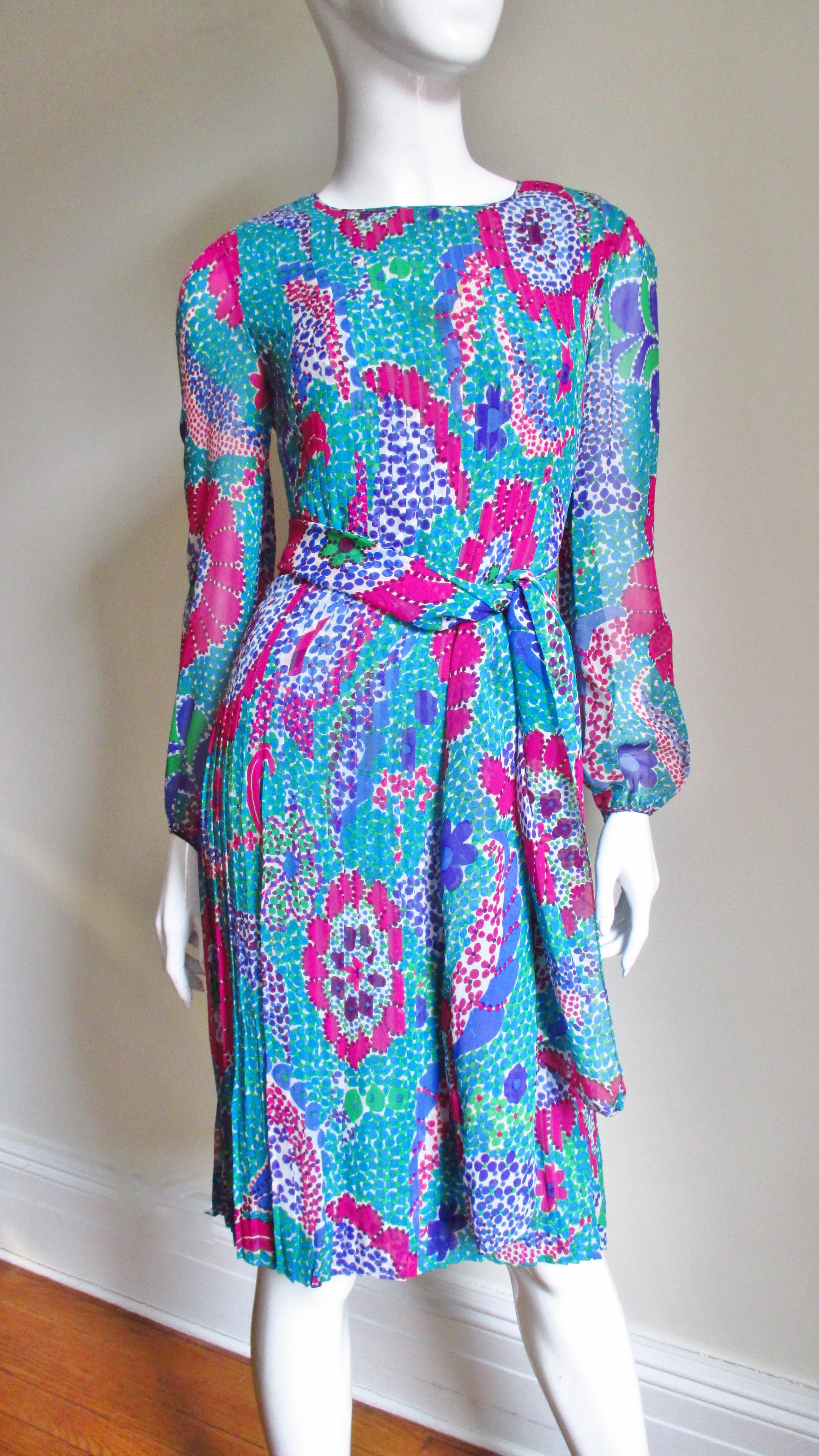 A fabulous 1960's silk dress from Pierre Cardin in a brightly colored abstract print in blues, green, fuchsia and white. It has semi sheer full sleeves which gather at the wrists. The body of the dress has elaborate vertical seaming extending from