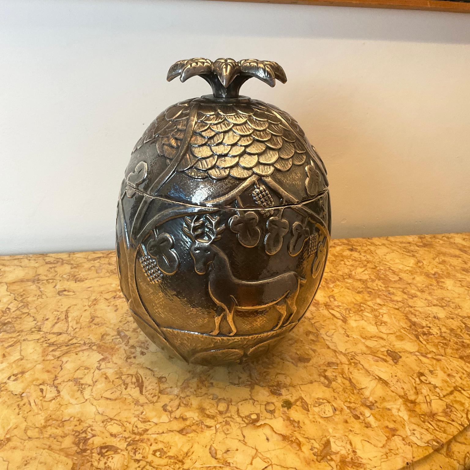 This pineapple-shaped ice bucket is decorated with embossed images of a camel, deer, and elephant surrounded by fruits, leaves, and branches, on its top lid is a lion's head
This decor is reminiscent of Naïve Art paintings such as the work of the