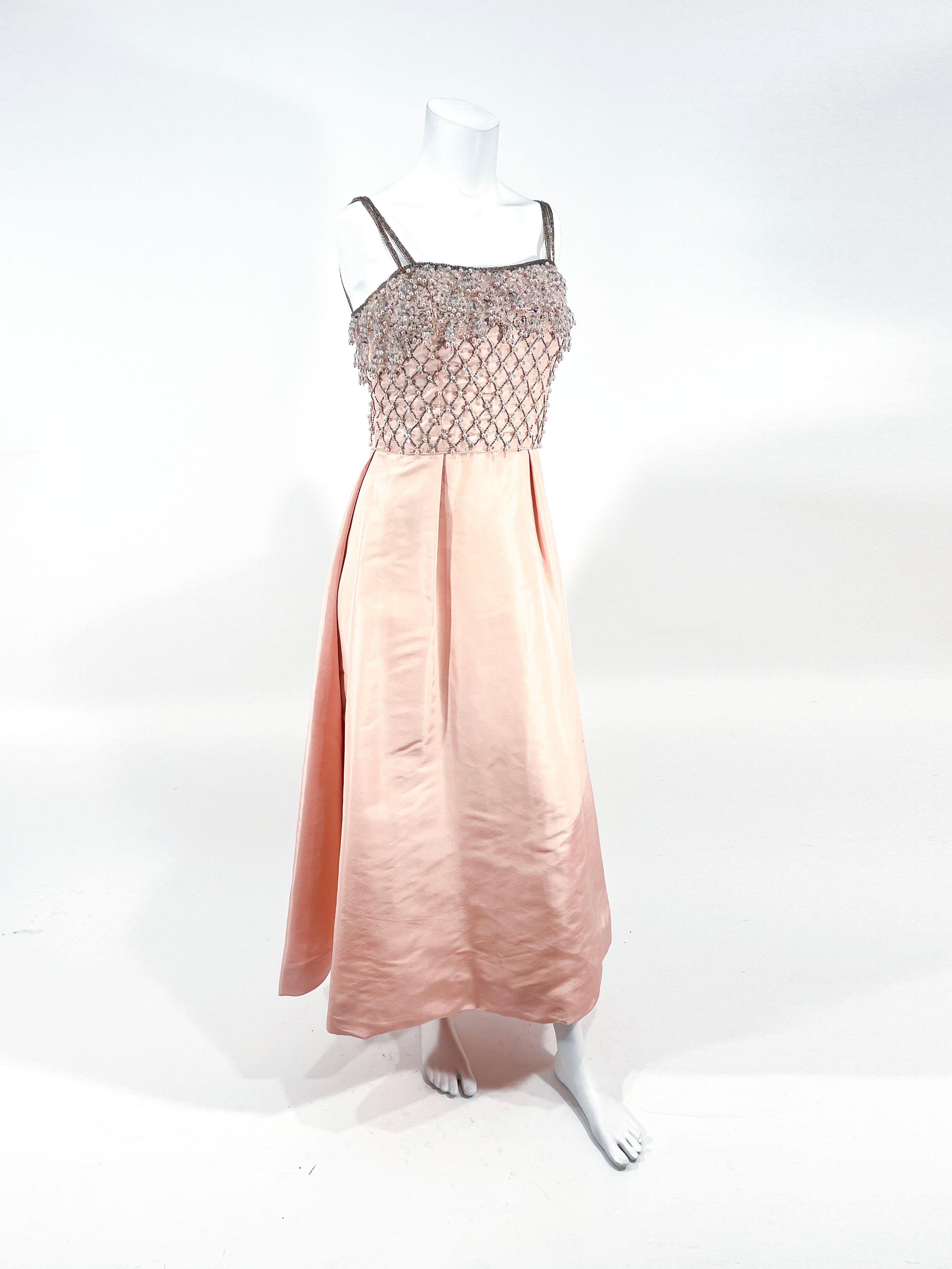 1960s Pale pink satin gown featuring a bodice adorned with beads, sequin, and hanging iridescent faux pearls. The interior of the bust is entirely structured and boned. The stain skirt is entirely faced to give the garment a full shape.