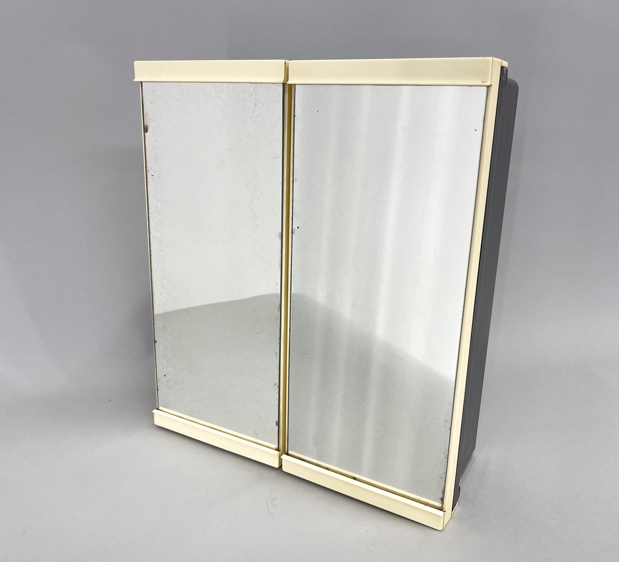 A popular 1960s cabinet with mirrored doors and shelves inside. Usually used in bathrooms. Made of plastic in black and cream colour. The mirror bears signs of time.