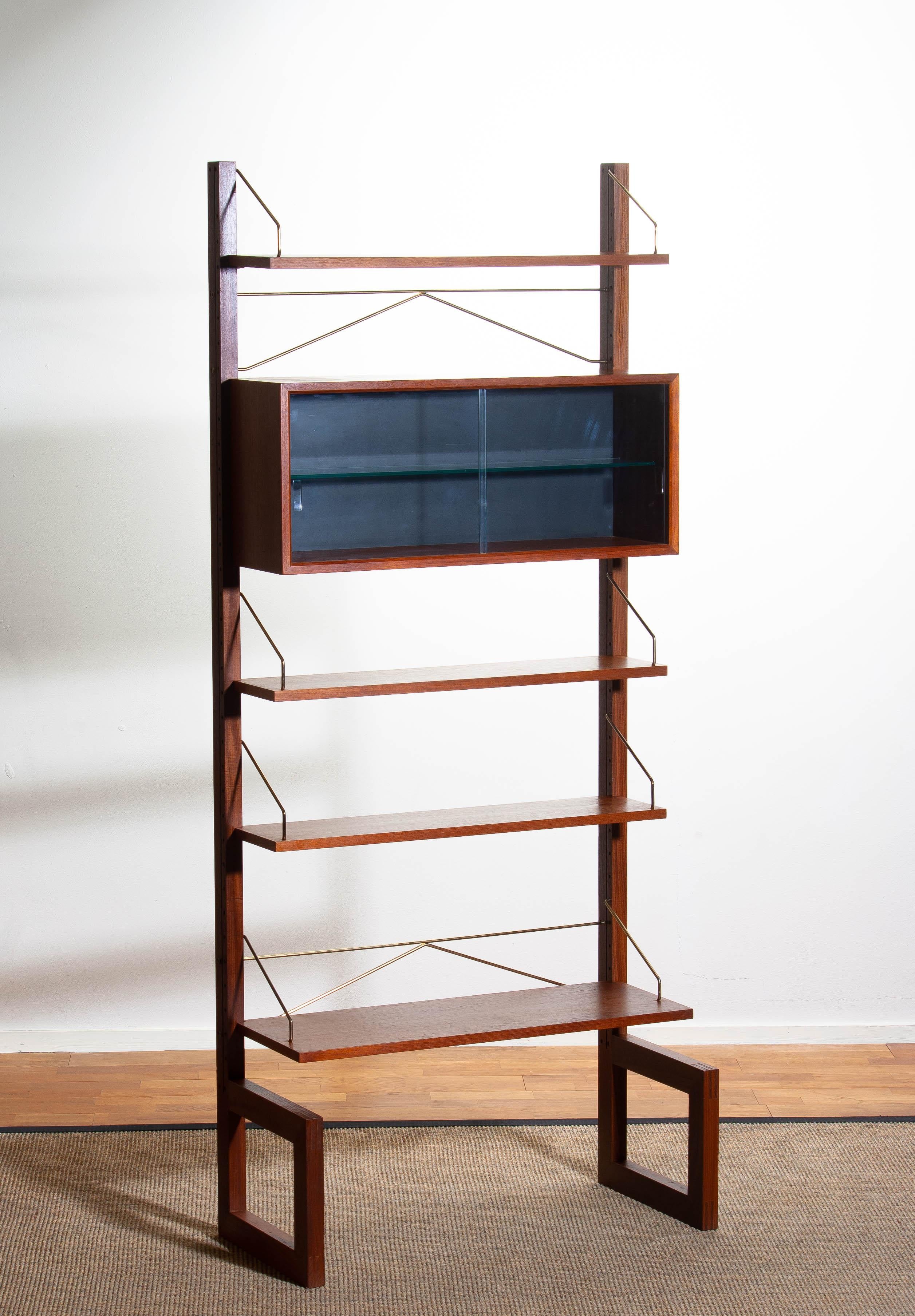 A beautiful and rare freestanding / wall unit designed by Poul Cadovius for Cado, Denmark. This cabinet is made of teak. 
Three bookshelves depth 20 cm / 8 inch.
One shelf depth 30 cm / 12 inch.
One vitrine with harden glass sliding doors and