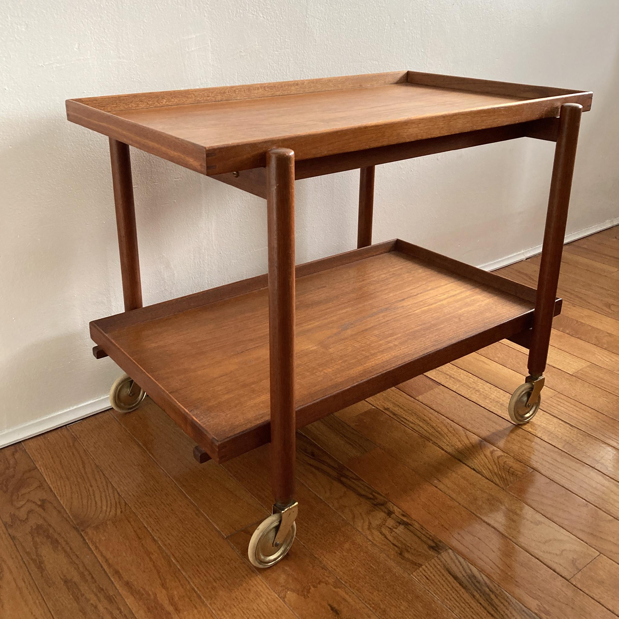 Danish Midcentury teak bar cart designed by Poul Hundevad for Hundevad & Co., featuring two tray tiers which can be removed and rearranged into a larger serving top. Beautiful, original gold metal casters accentuate the teak.

Measures: H 23.5