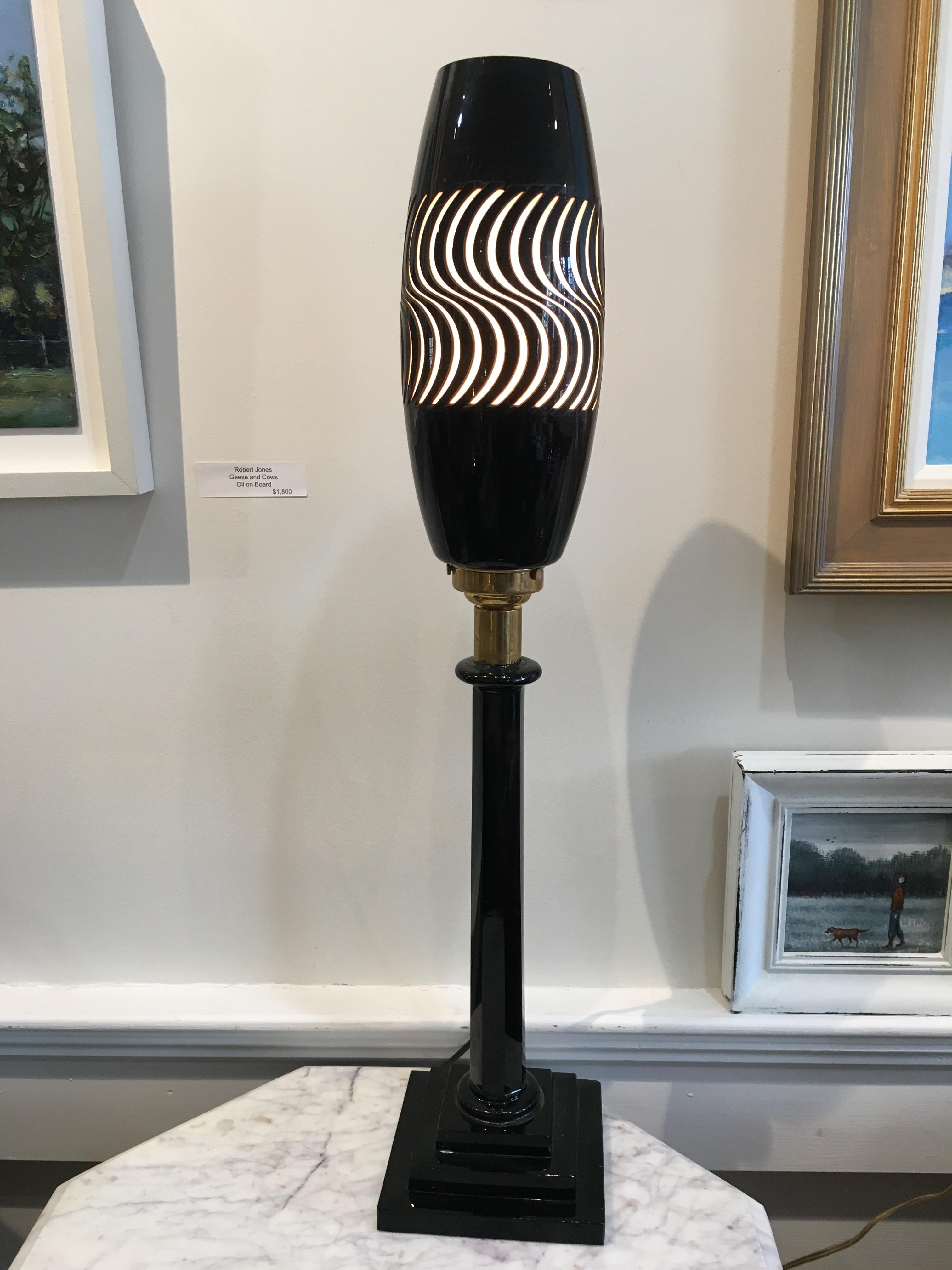 A very cool 1960s psychedelic table lamp in black glass and brass. Most of the lamp is black glass including the base, and brass where the light fixture component attached. The black glass shade has been cut away making a cool pattern that is backed
