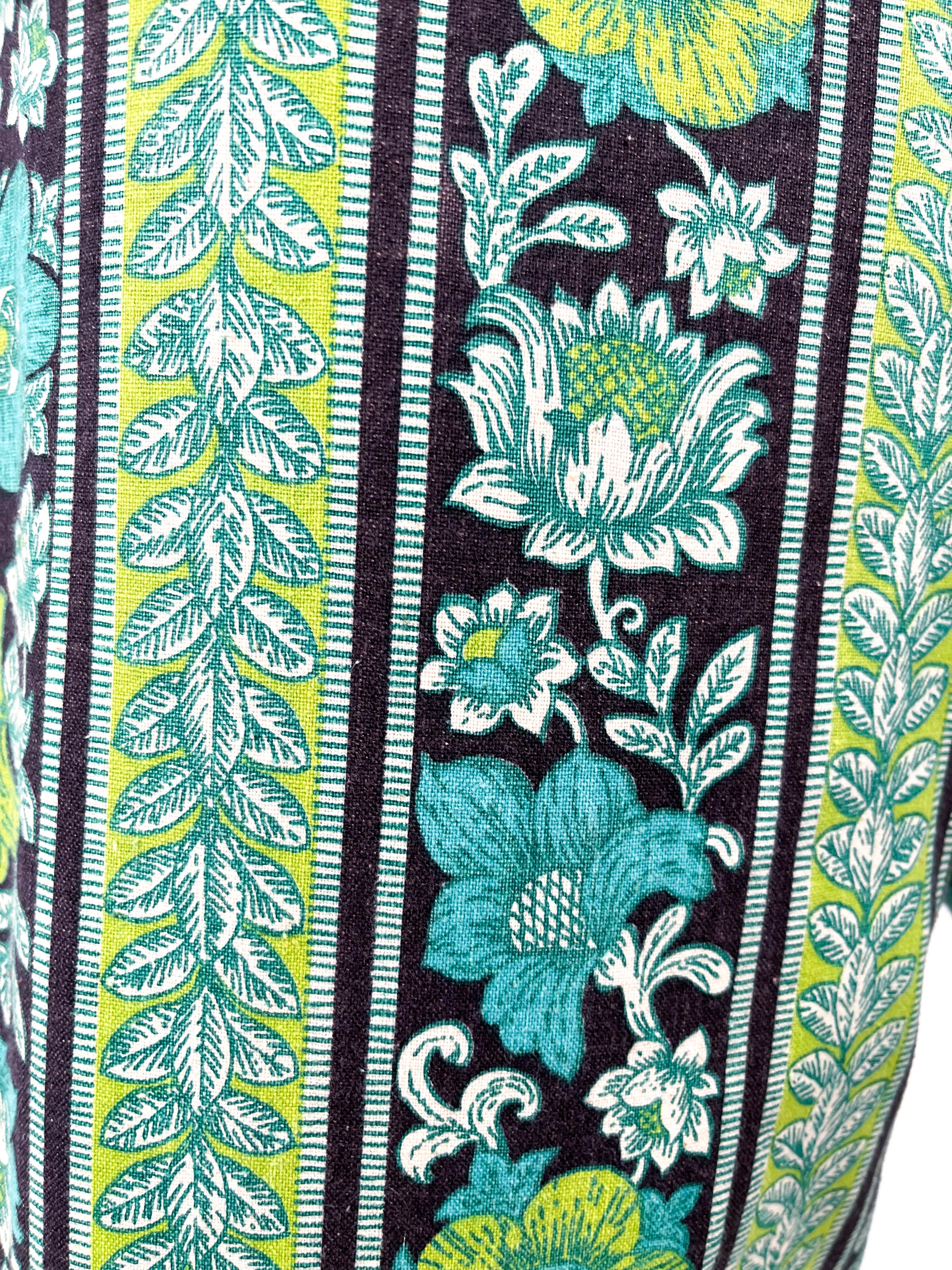 Psychedelisch bedruckte Schlag- und Bundhose aus den 1960er Jahren. Der florale, psychedelische Druck zeigt neongrüne, blaugrüne, schwarze und weiße, gestreifte Motive. Die niedrig geschnittene Taille hat passende Gürtelschlaufen und einen