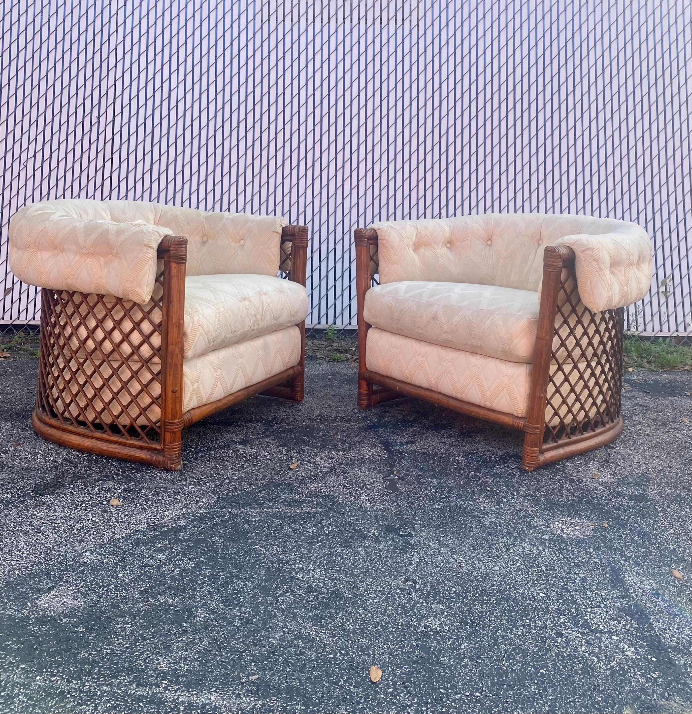 A pair of Mid Century tub barrel chairs by JD Originals. The rattan finished frames are upholstered in beige with button-tufted details on the backs and arm panels. Beneath the chair cushions, the fabric is marked ‘JD Originals’. The chairs are