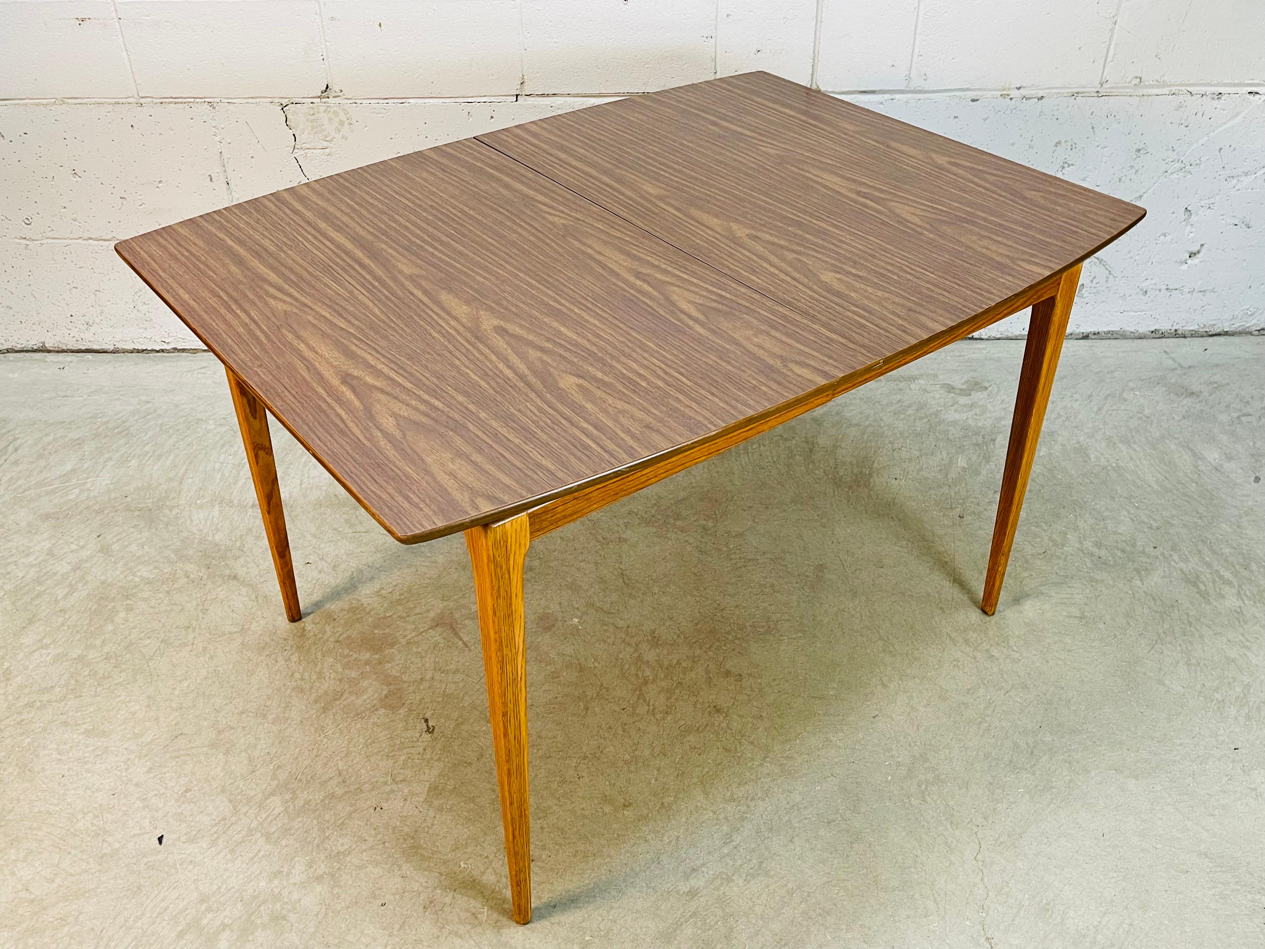 Vintage 1960s rectangular dining room table with a solid oak wood base and formica top. The table is solid and sturdy and comes with a single extra board. The board is 11.25”W. In newly refinished condition. No marks.