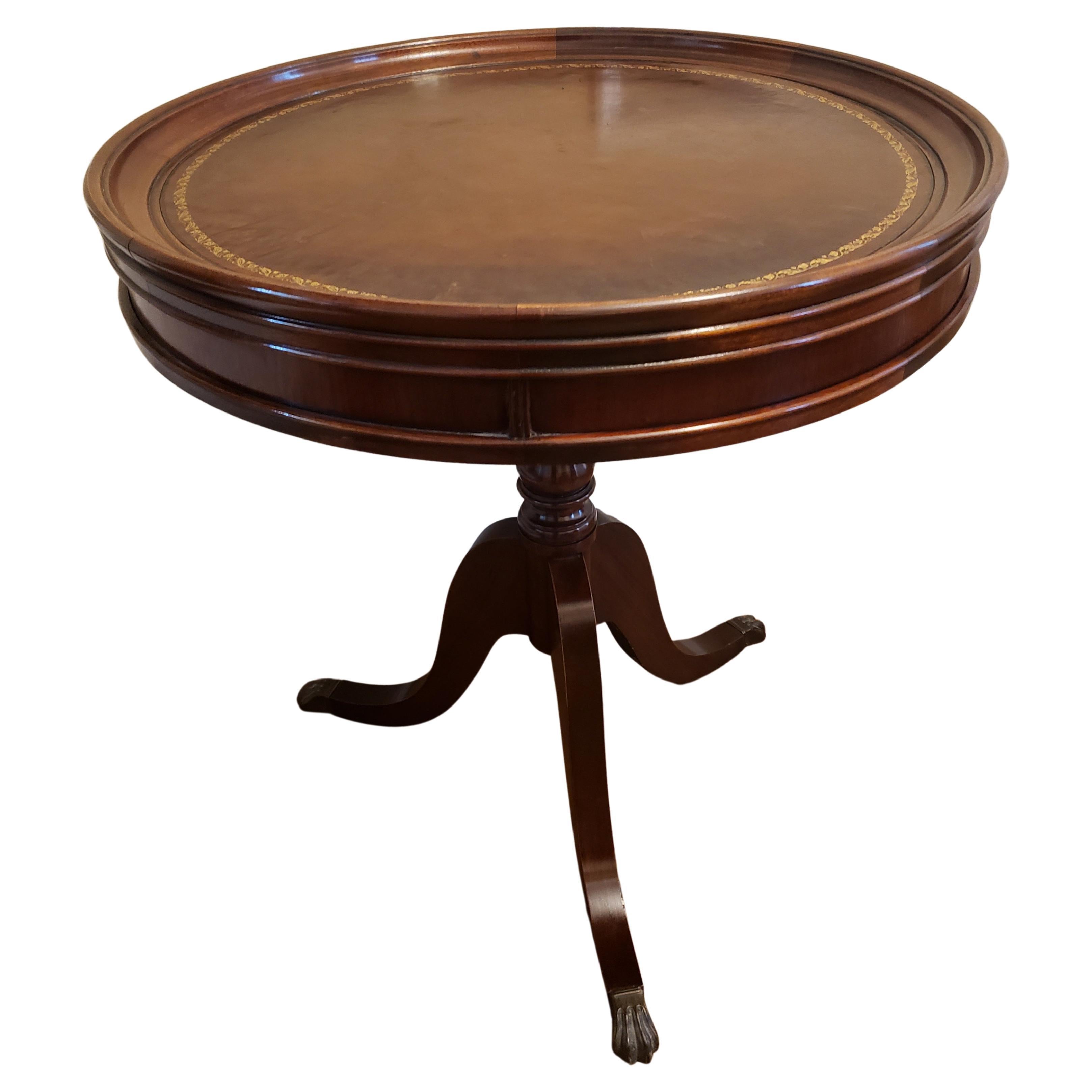 A well kept 1960s Regency Mahogany and Tooled Leather Stencil tripod Pedestal Tea Drum Table with brass paw feet. Measures 25.5