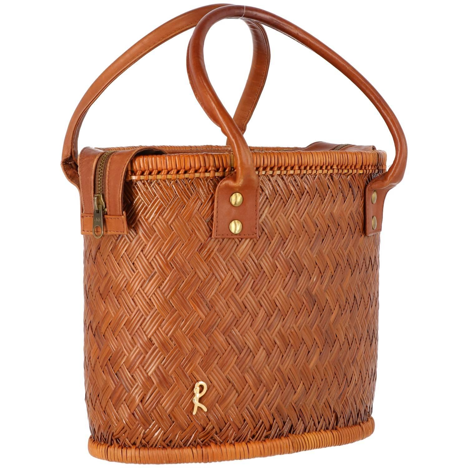 Vintage rattan bucket bag from the 1960s, with leather handles and closing surface. The inside features a lining with an applied pocket. A golden metal brand logo is applied on the front.

Handle Width: 13 cm
