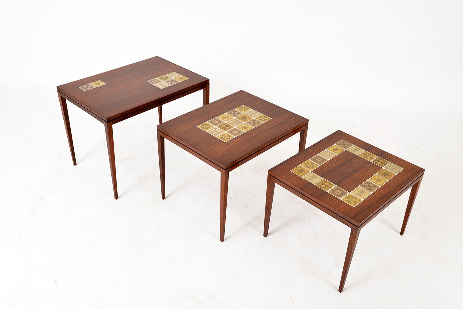 Stunning nest of three side tables of receding heights by Rosenthal Domus, each with a different arrangement of porcelain tile inlays from Bjørn Wiinblad’s Quatre Couleurs design in exuberant tones of gold on a white glaze. All three tables bear the