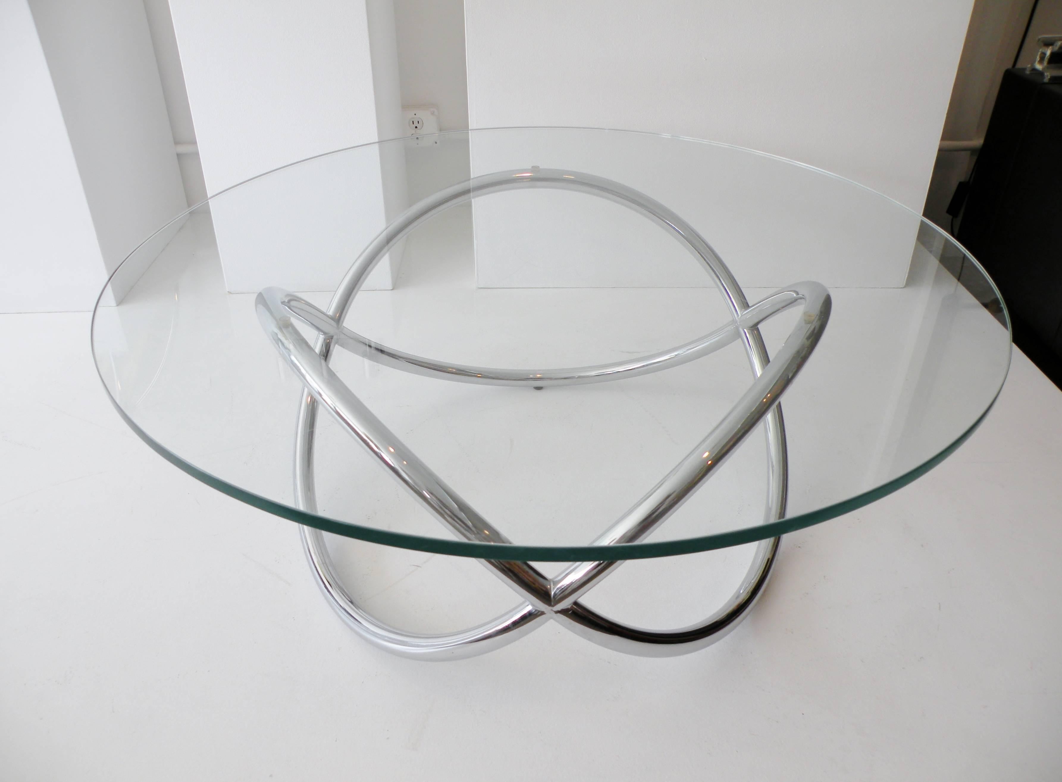 Sculptural modernist chrome and glass round coffee table. A knotted tubular pretzel twist chrome-plated base 27