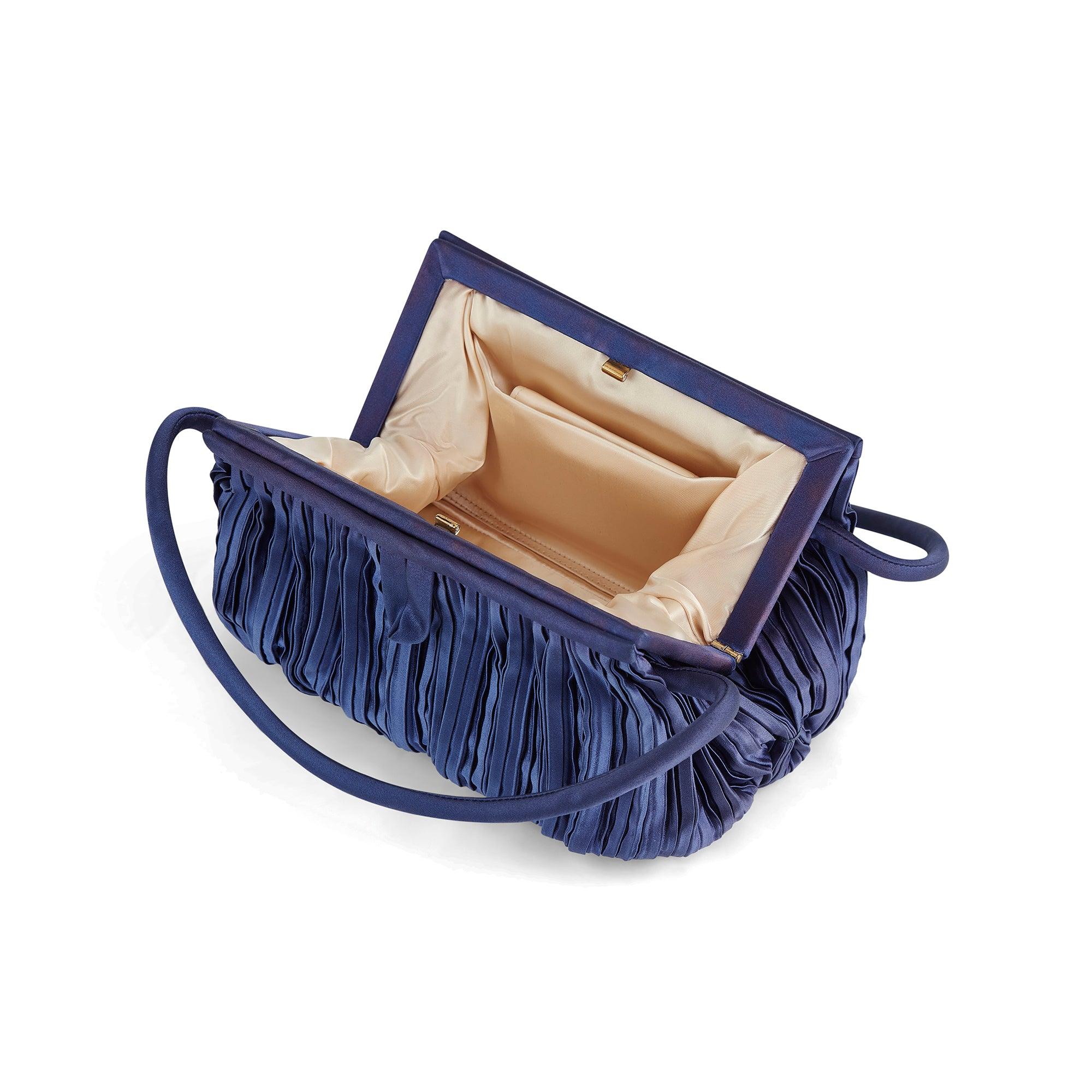 This 1960s top handle bag is crafted from a rich, blueish-purple silk satin and pleated all-over with swirling forms across its base where the pleating gathers. It has a structured top with a gold-toned metal clasp closure inside. There are fabric