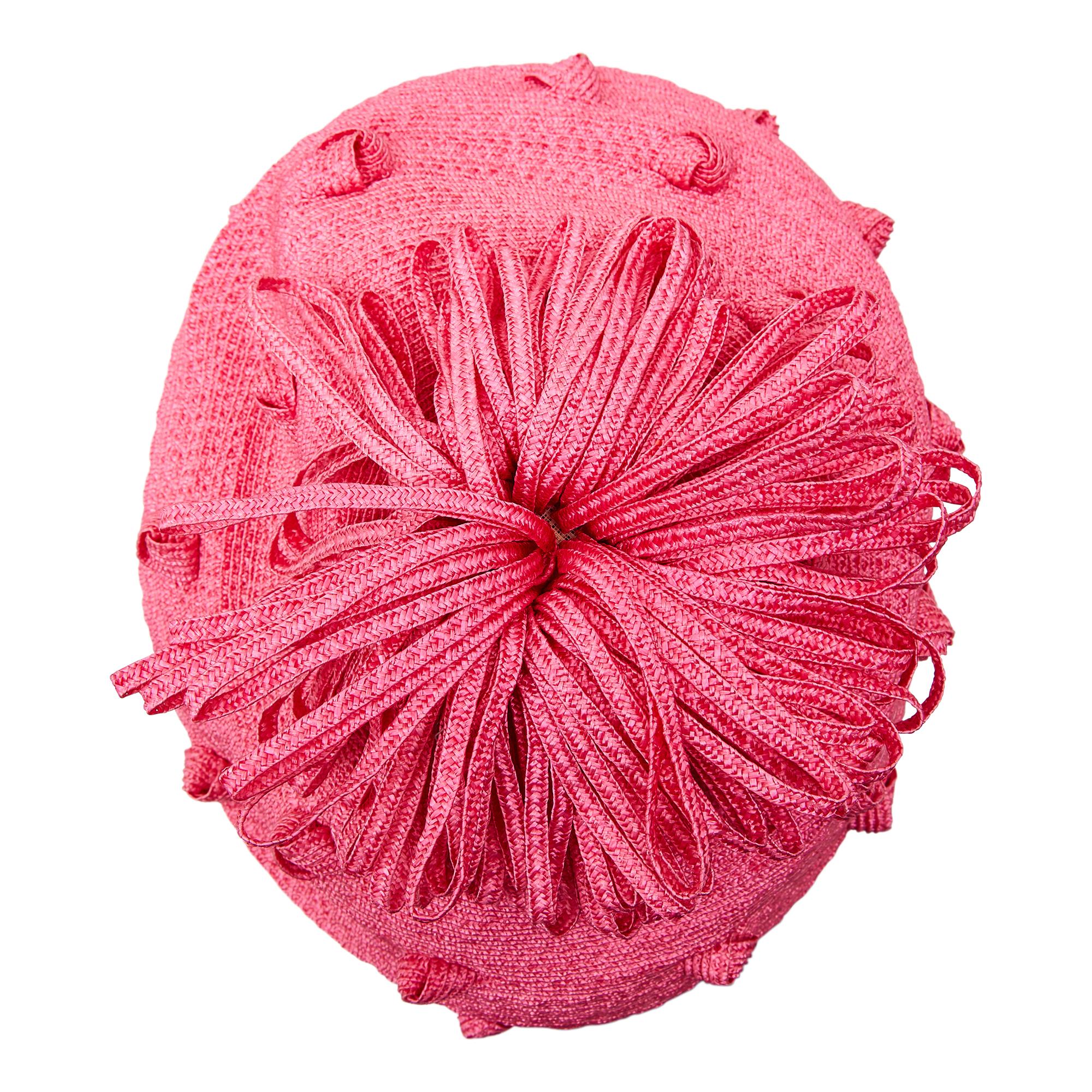 Si tratta di un divertente cappello di paglia di Simone Mirman risalente agli anni '60. La paglia è di colore rosa bubble-gum, con nodi stravaganti e un pom pom con bordo a volant applicato sulla parte superiore della corona. Questo cappello può