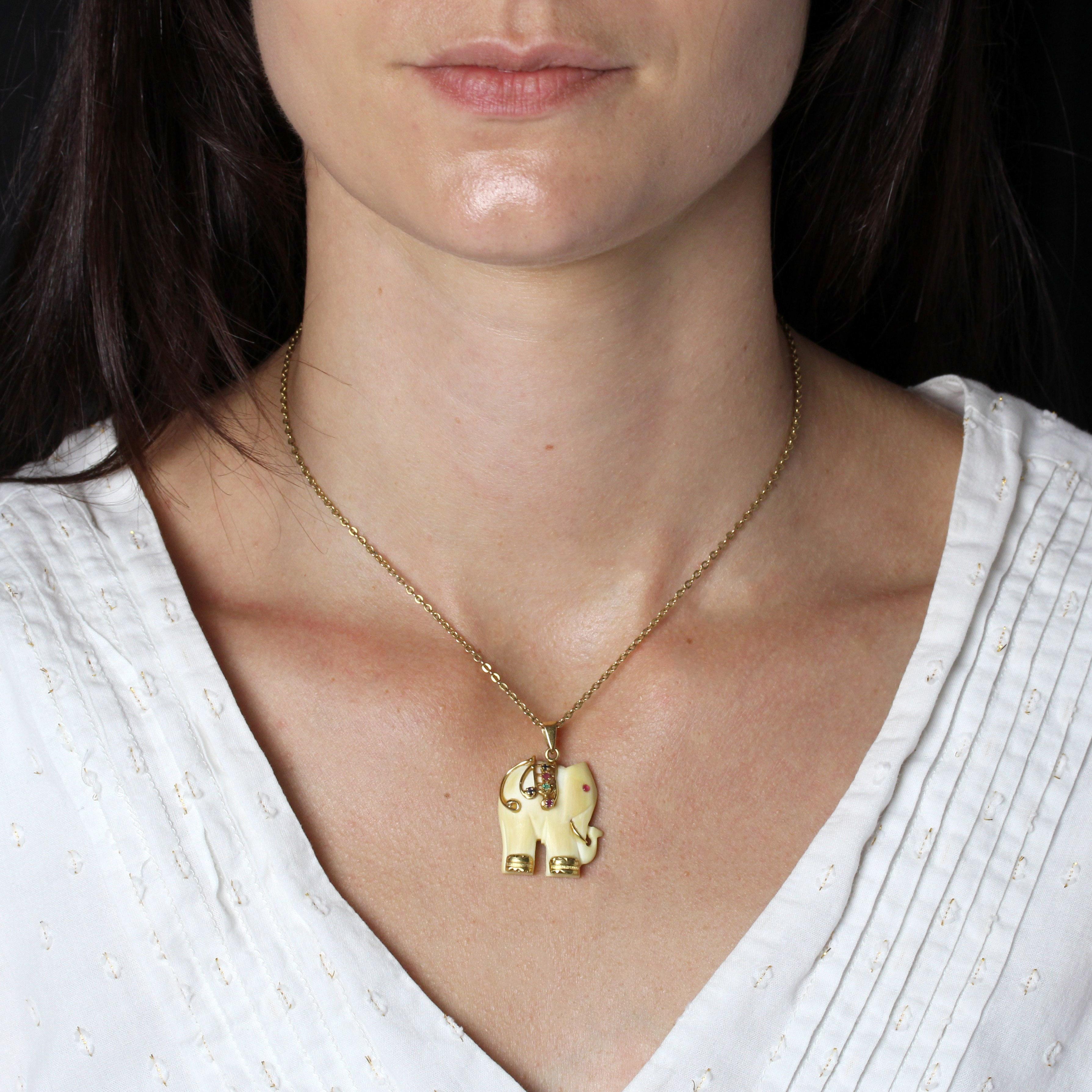 Pendant in 14 karat yellow gold.
This antique pendant features an elephant carved from bone. Its tusk, tail and legs are in gold, its back is adorned with two rubies, two sapphires and an emerald, and its eye is set with a red cabochon