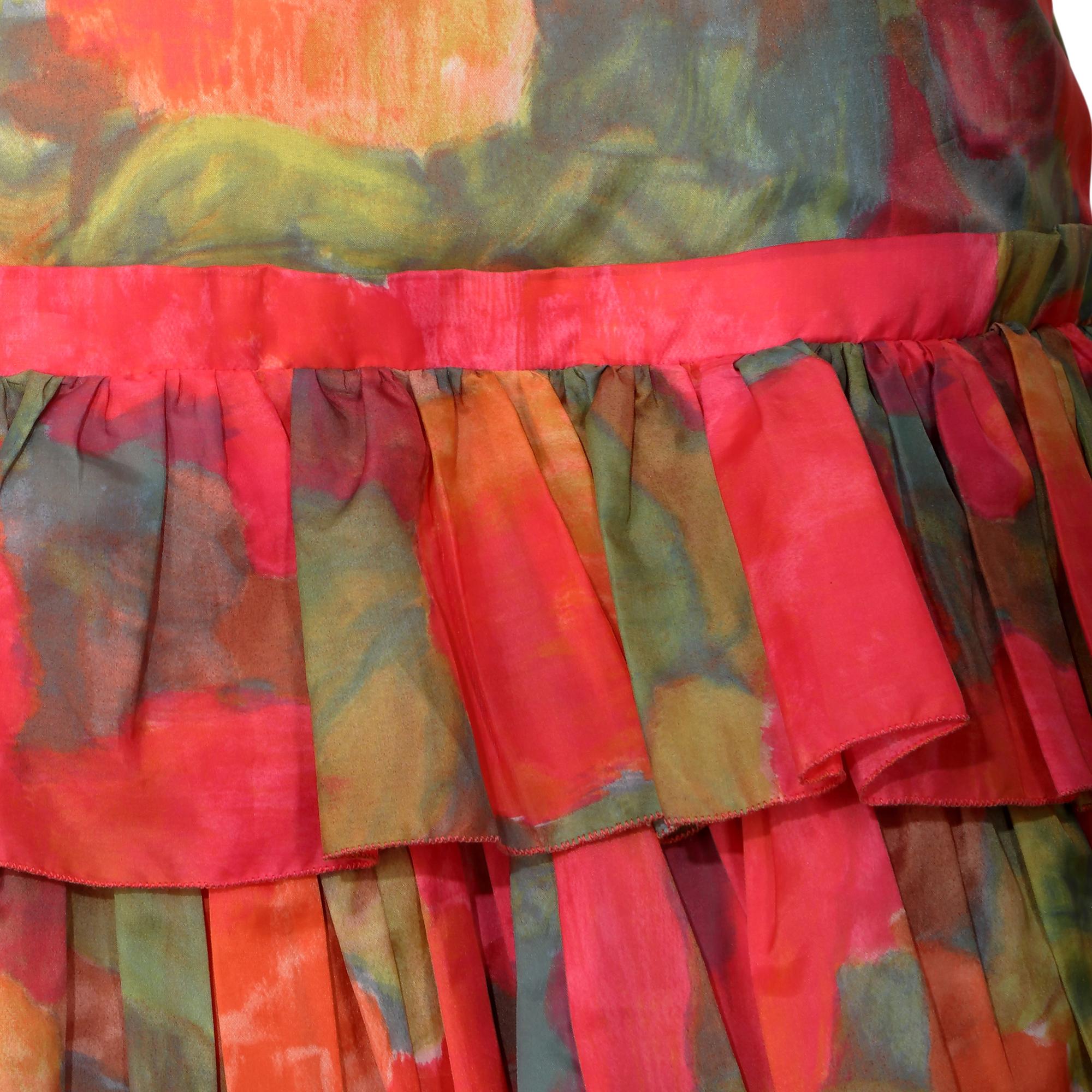 Dieses originelle Vintage-Kleid aus den 1960er Jahren besticht durch seine leuchtenden Farben. Es scheint ein abstrakter Rosendruck in warmen Rosé-, Orange- und Grüntönen zu sein. Das herausragende Designelement dieses Stücks ist der wunderschöne