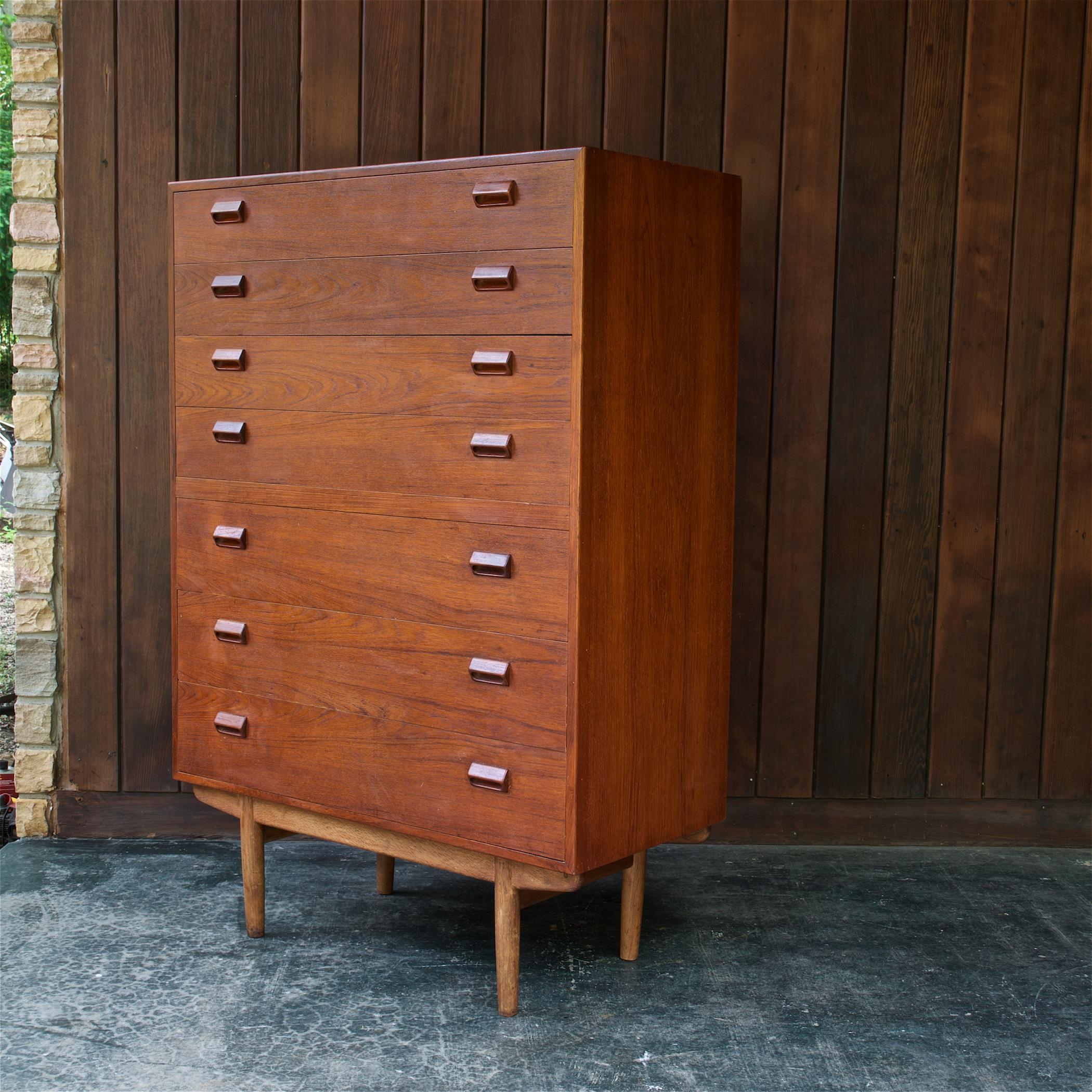 More uncommon model from Borge Mogensen, a 7-drawer tall teak chest of drawers on solid oak turned wood sled style base. Retains label to verso, made by Soborg Mobler. 

This dresser is in fair vintage condition, it is showing wear on most surfaces;