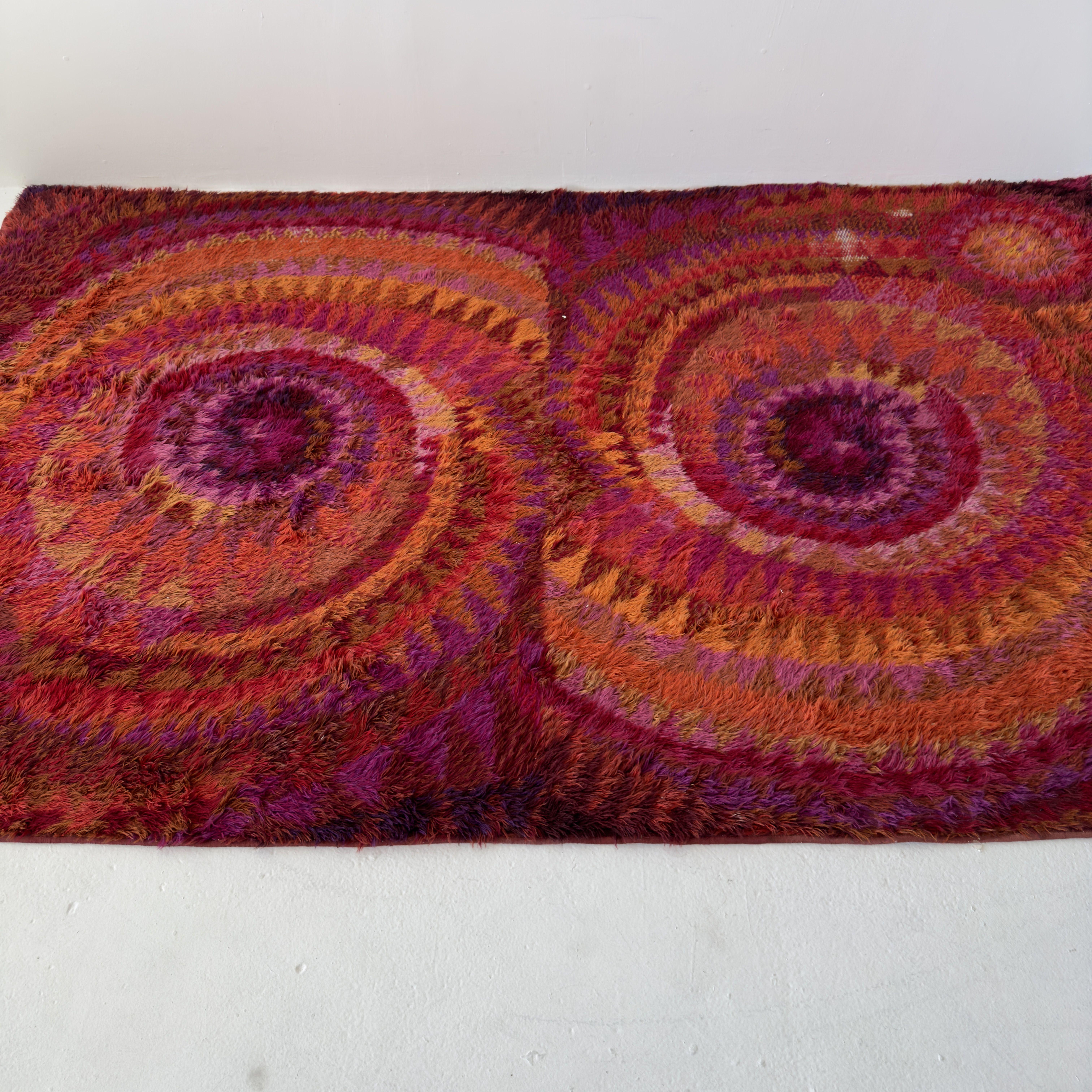 1960s rya rug by Finnish textile artist Marjatta Metsovaara, approx 6x9 feet. A happy, kaleidoscopic pinwheel of magents, reds, pinks and oranges. Good vintage condition with heavy wear on one section (pictured).

L108 W67

This vibrant 1960s rya
