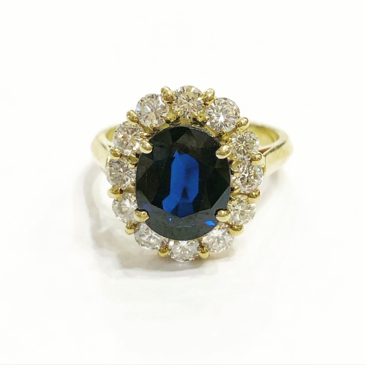 Klassischer 1960er Jahre, ovaler Saphir und Diamanten Halo Gelbgold Cluster Verlobungsring.
Ein klassisch gestalteter Ring aus 18 Karat Gelbgold mit einem ovalen blauen Saphir, umgeben von runden Brillanten. Dieser oft als Prinzessin-Diana-Ring