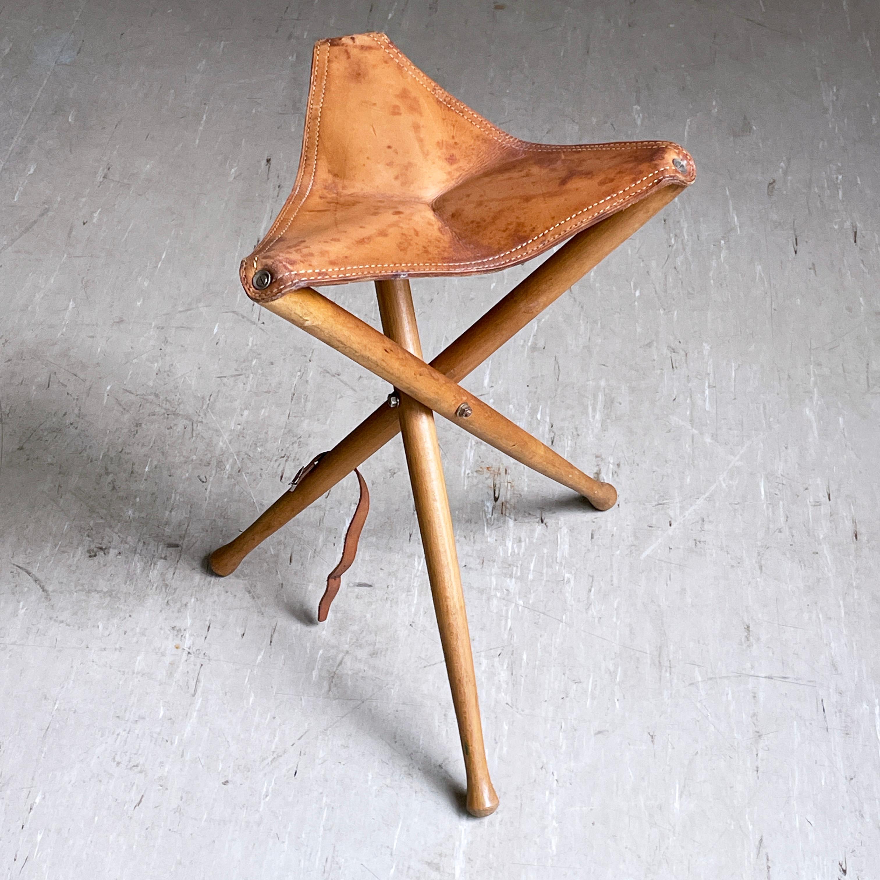 Vintage 1960's Skandinavisch Safari Hocker. Massiver Buchenholz-Dreibein-Sockel mit originalem dickem Ledersitz (Patina auf Leder). Zusammenklappbar mit Lederschnallenriemen für leichteren Transport und Lagerung. Völlig stabiler Aufbau und ideal für