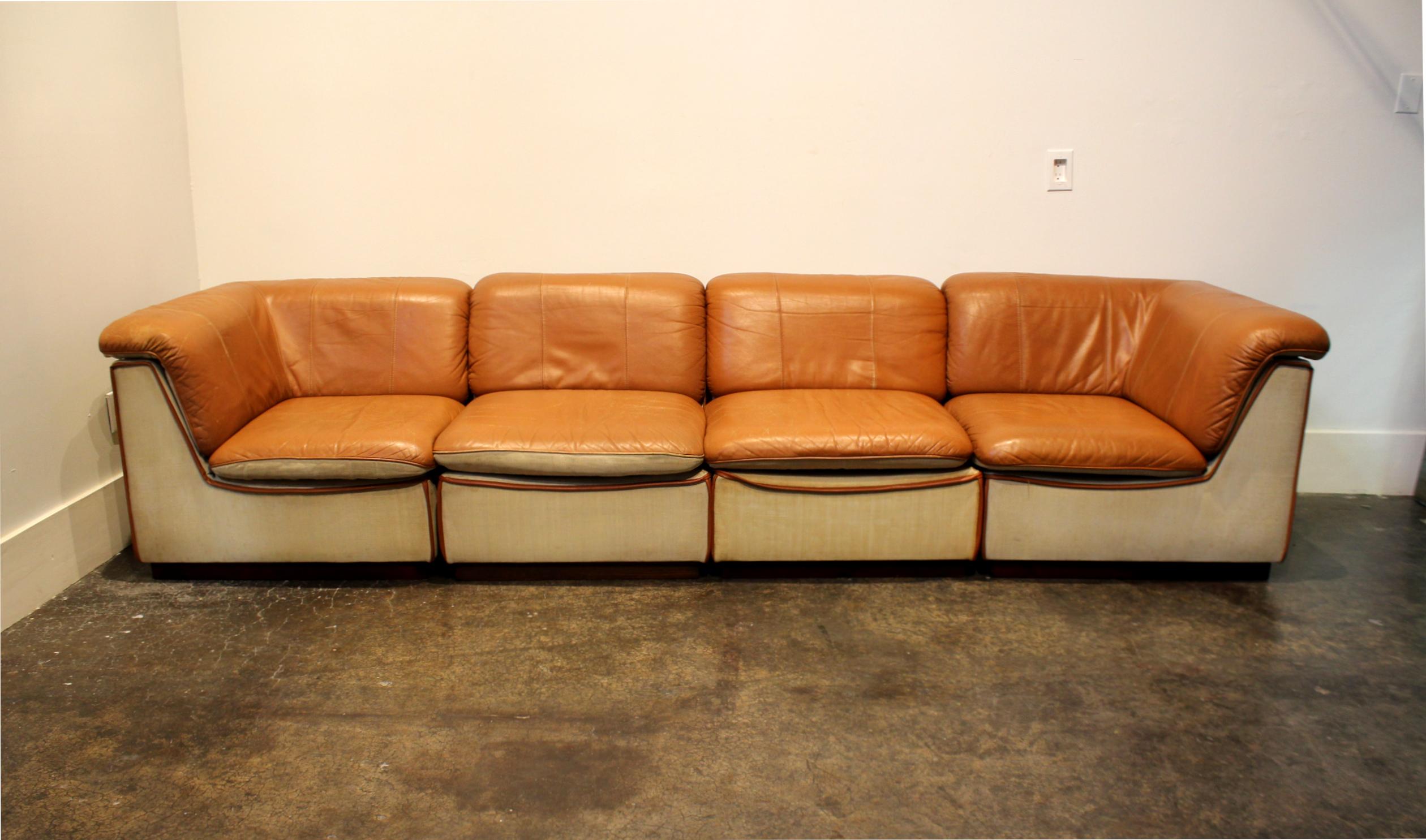 Massive and endlessly changeable modular sofa composed of two corner pieces, two side pieces and one ottoman on metal casters. Cognac/tan leather tops with linen sides raised on walnut wood plinths. Total length is over 10 feet. Same model (possibly