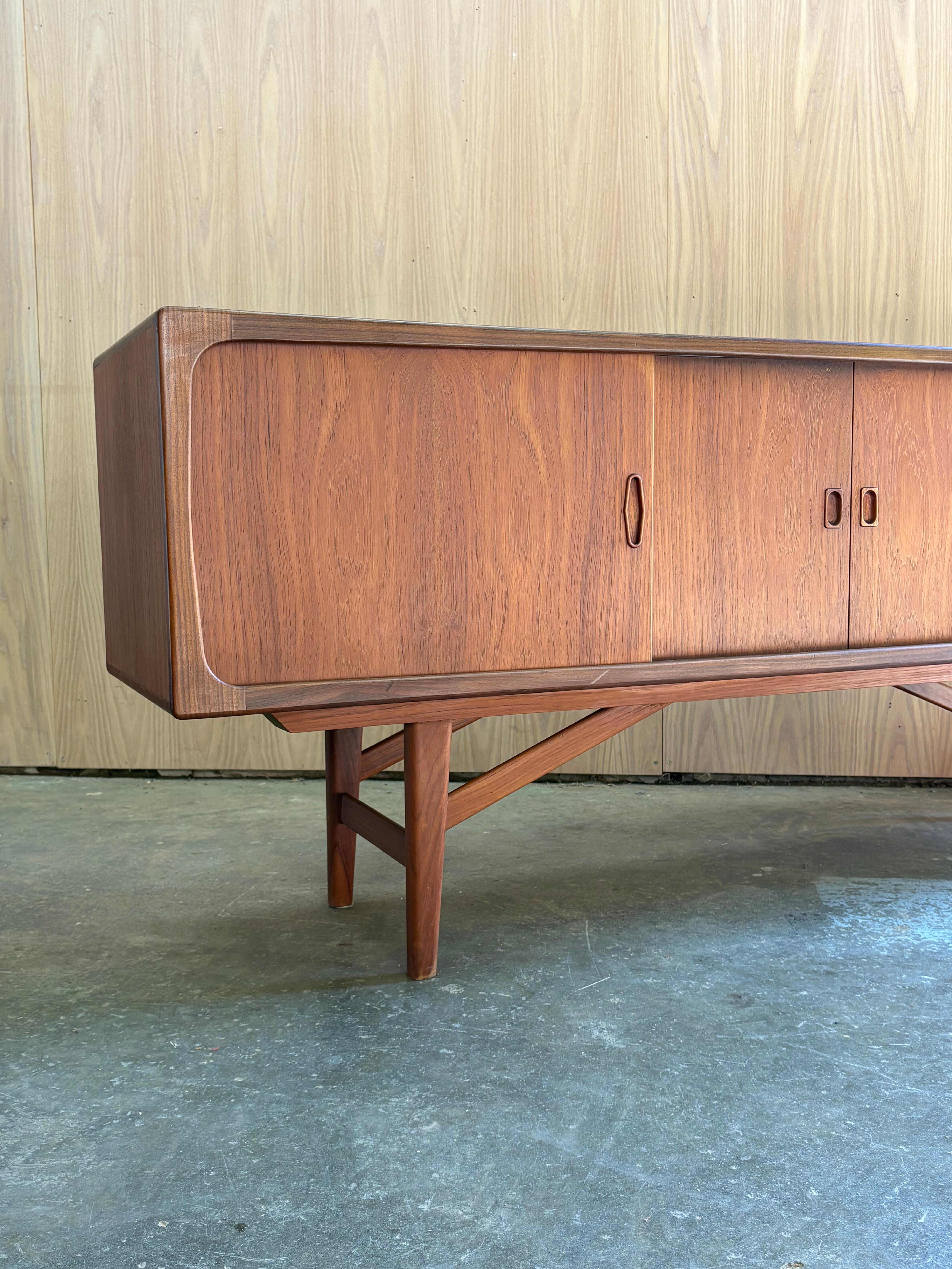 Exemple remarquable du design scandinave, cette crédence en teck des années 1960 est un chef-d'œuvre de proportions, de détails et de savoir-faire. Le cadre sculpté repose sur une incroyable base angulaire - une construction de haute qualité à la