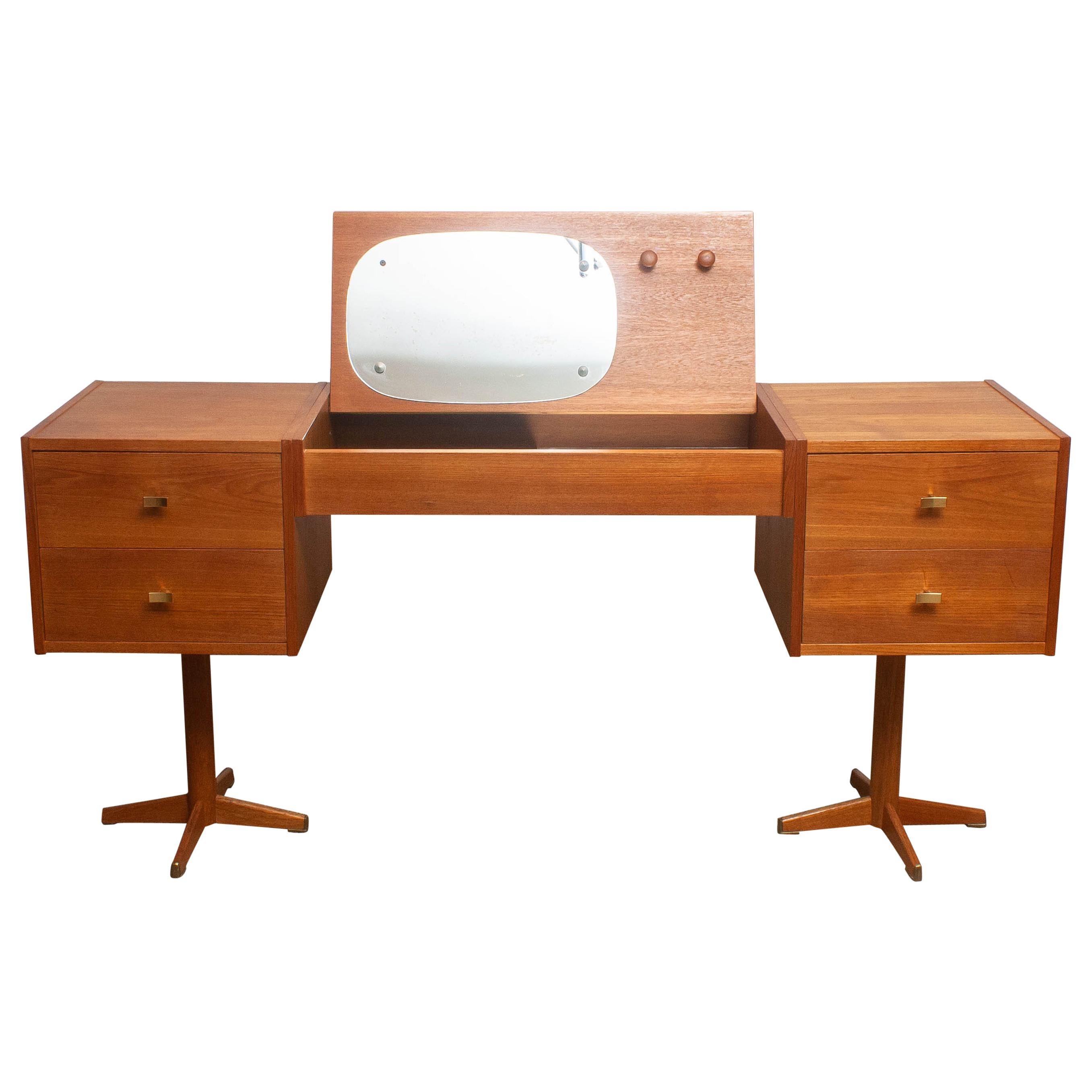 Beautiful vanity desk made in Scandinavian Sweden.
This piece is in a very nice and good condition.
It is made of teak with four drawers with brass handles and in the top a flap with storage space and mirrors and hanging knobs.
The legs are