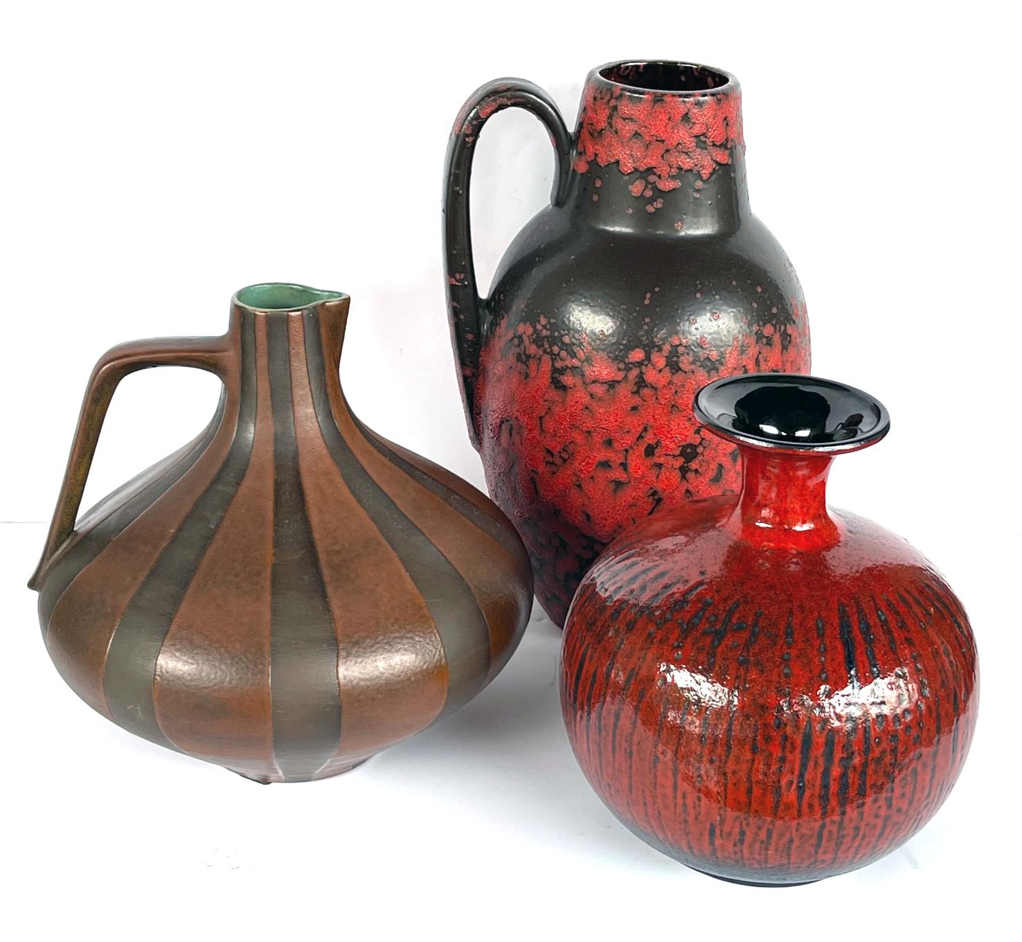 With cylindrical spout above a bulbous body adorned overall with a fiery red-lava-over-brown glaze.