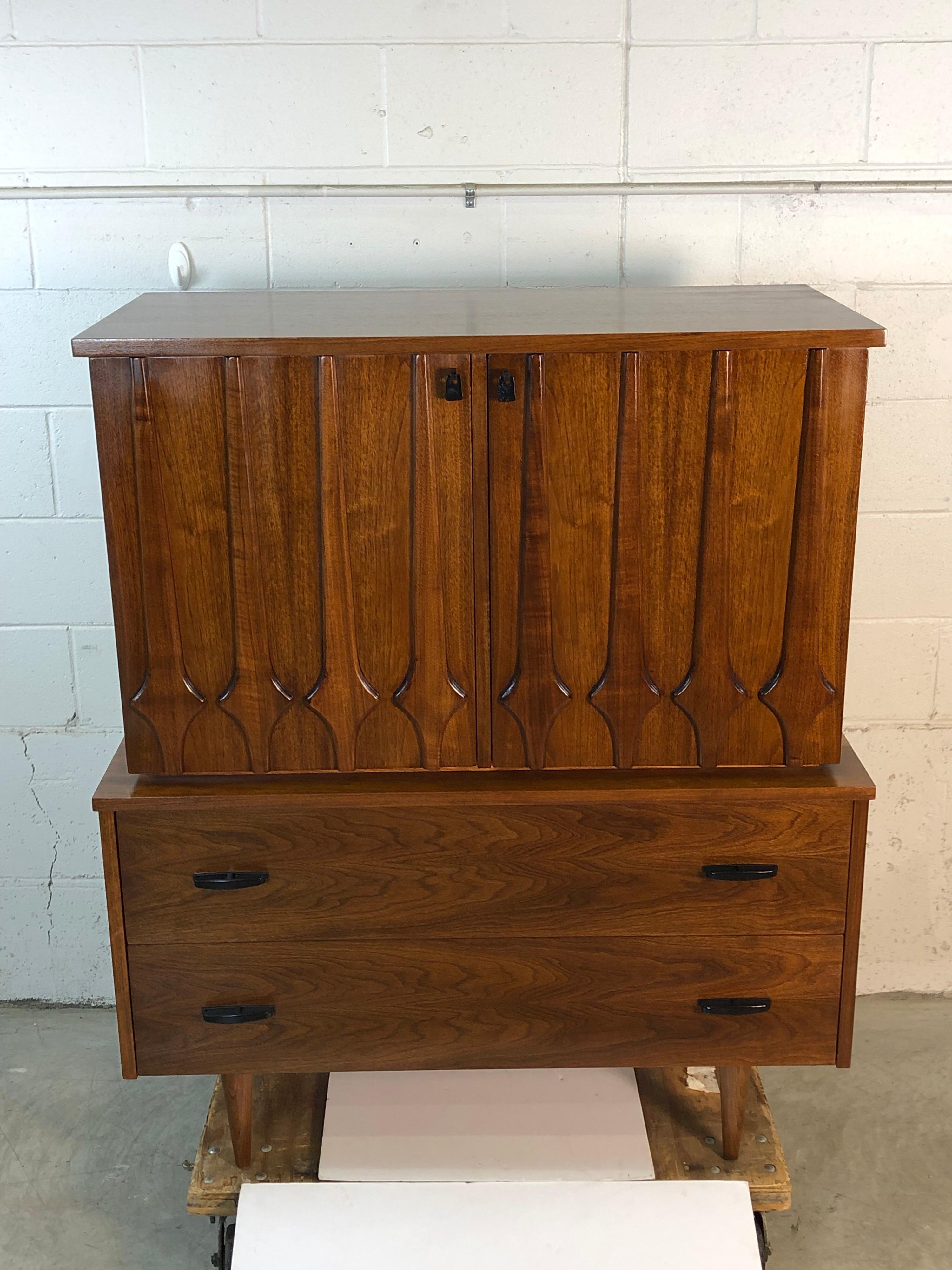 Vintage 1960s walnut sculpted front tall highboy dresser with eight drawers. The top has six drawers and the bottom has two drawers. All the drawers are deep and can hold a lot of items. This is one a piece dresser. The dresser is newly refinished