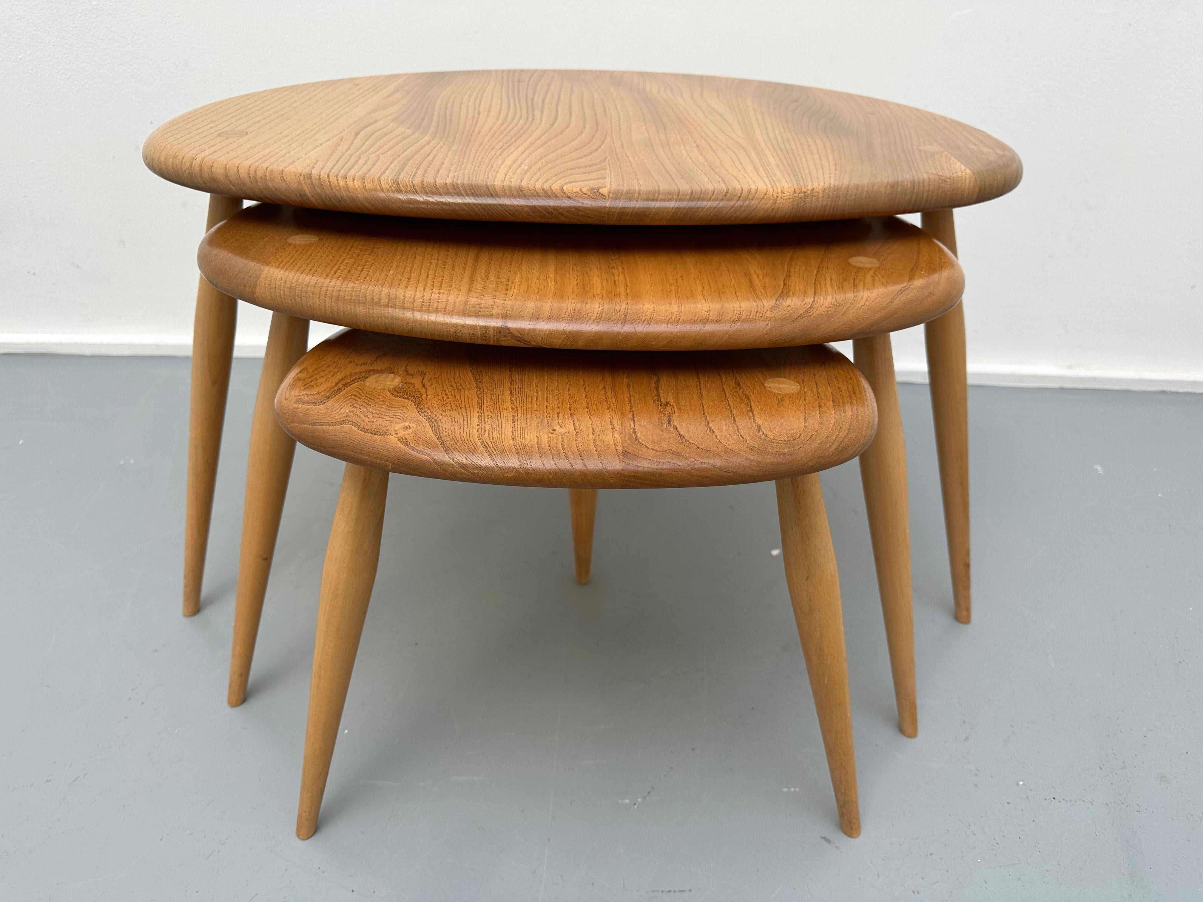 1960s Ercol nest of three 'Pebble' shaped coffee or side tables. Model 354. The table tops are constructed from planks of English Elm and the legs in Beech. This design classic consists of three individual tables, each one sliding neatly underneath