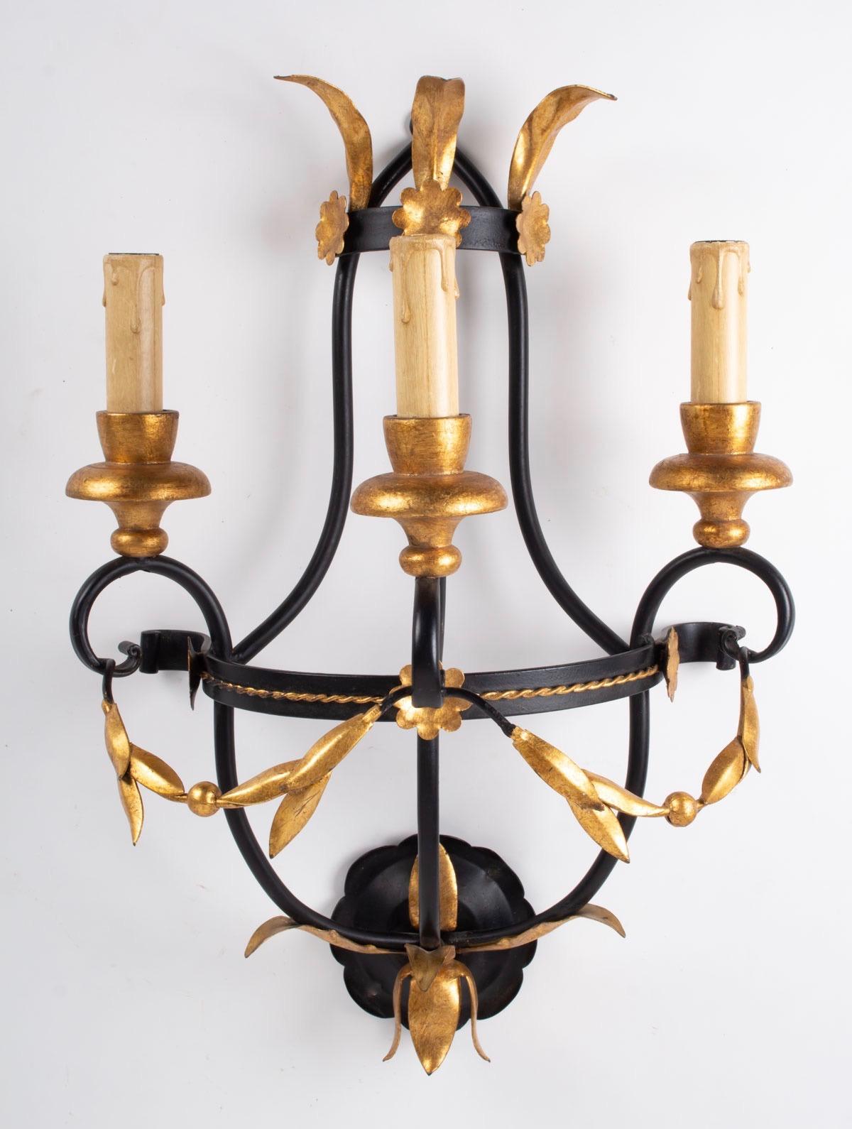 1960s set of 3 Maison Honore neoclassical sconces

The sconces structure is made of black lacquered steel stem. 
The 3 lighted arms are adorned with gilded leaves flowers and cups.
