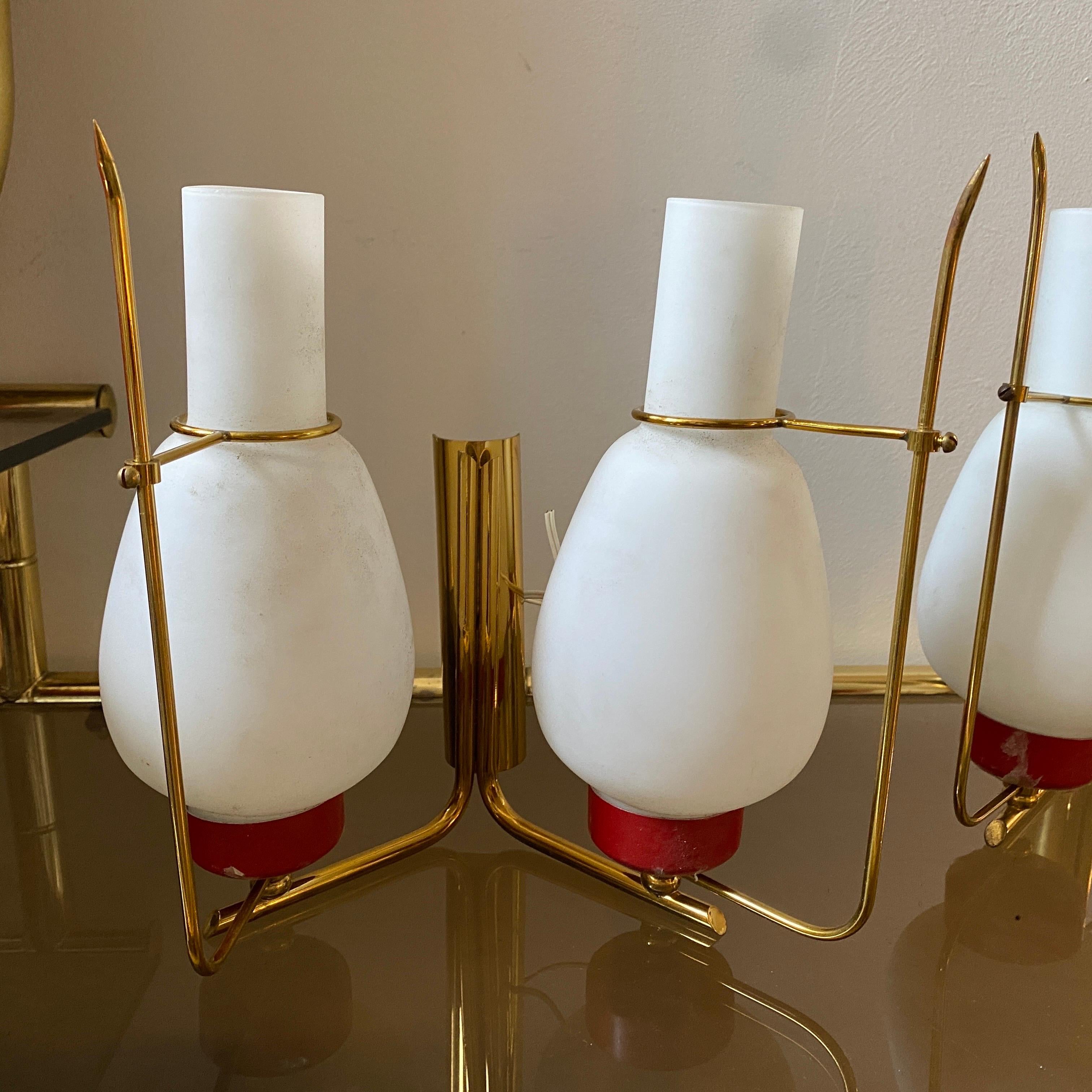Two elegant brass, red painted aluminum and opaline glass wall sconces designed and manufactured in Italy in the Sixties in the style of Arredoluce. They are in lovely conditions, they work both 110-240 volts and need regular e14 bulb.