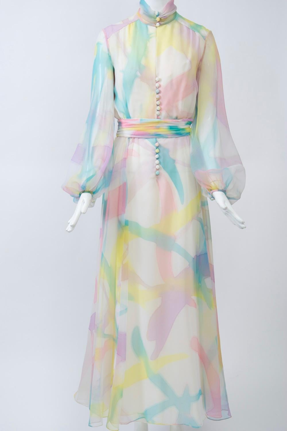 Sheer gauzy gown in an abstract, pastel, watercolor design featuring self buttons and loops down the front with a keyhole bodice and balloon sleeves fastened at the wrist with a matching button. The high, shirred and buttoned neck is mirrored in the